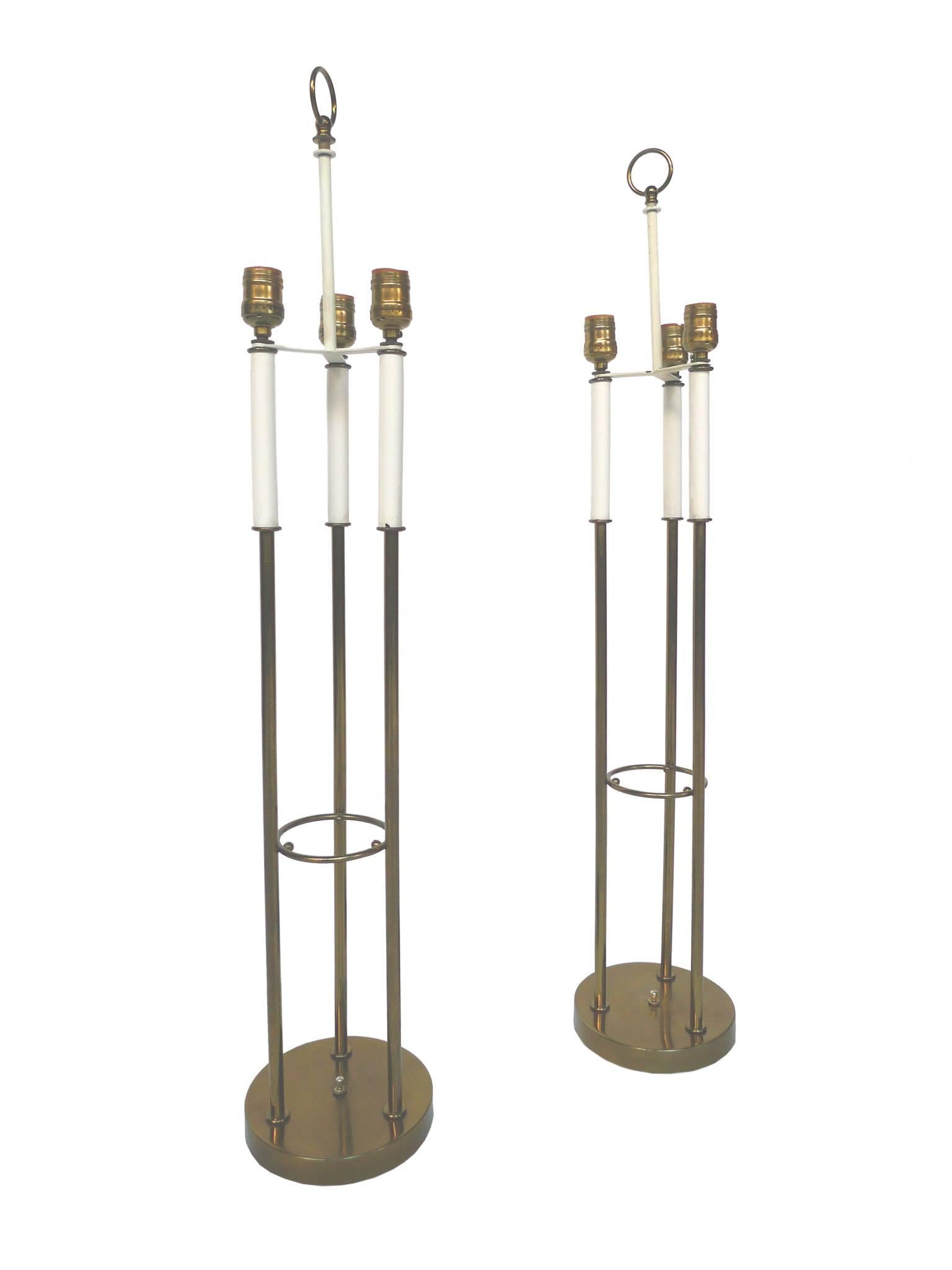 These Midcentury table lamps are each comprised of a brass body, three candlestick sockets and new parchment shades. Crafted in the style of Tommi Parzinger, the lamps are minimally designed but Stand out for their decorative brass-work. They have