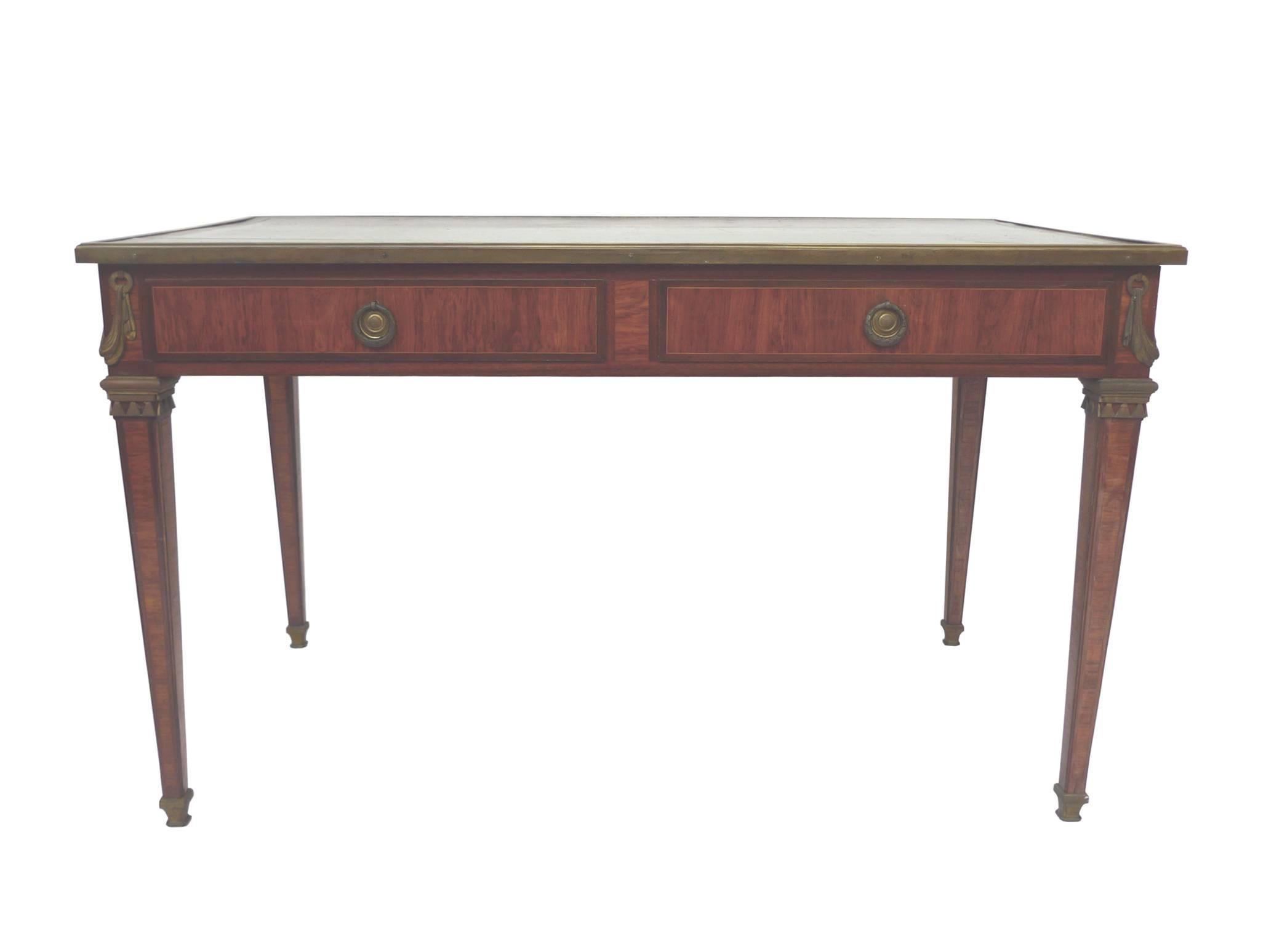 This French late 19th century writing desk is Cuban mahogany veneer. The top is covered in a beautifully aged, red-brown leather with embossed, gilt details and bronze trimming. There are two wide drawers with round pulls. The legs are also adorned