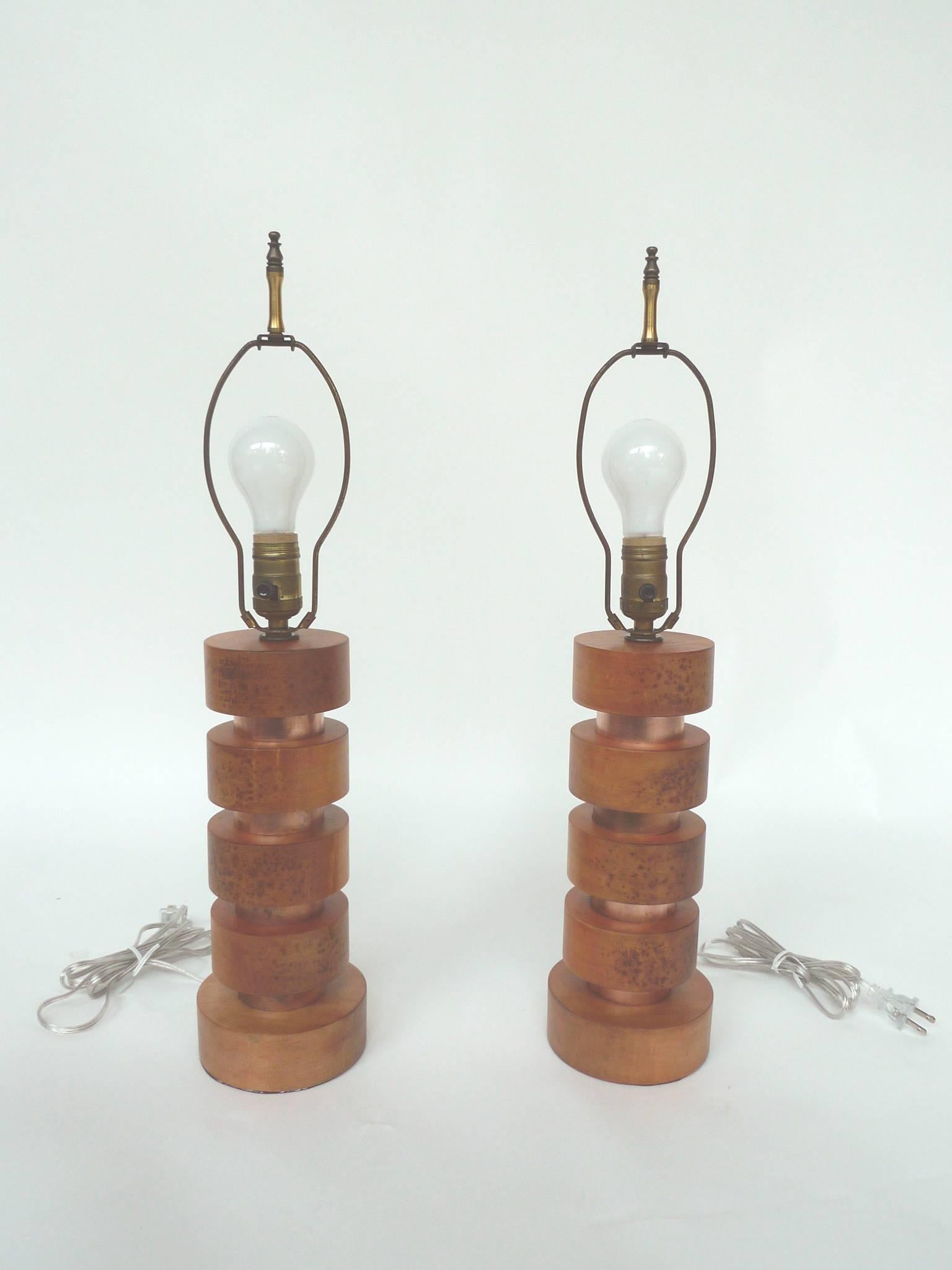 This pair of table lamps is in the style of Art Deco designer Paul Frankl. The wooden discs are newly refinished in rose and copper. The lamps have brass hardware and are rewired with single-bulb sockets. They are paired with new parchment shades.