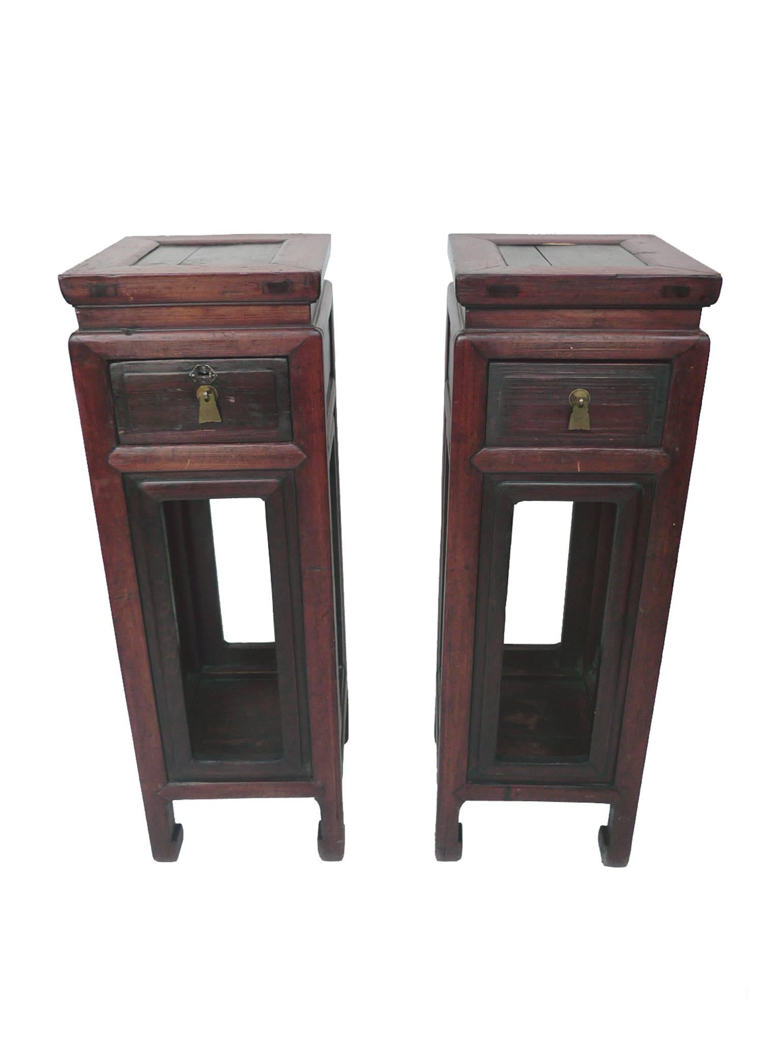 These 19th century, Asian pedestal stands are elmwood with a burgundy-red finish. The wood has aged beautifully, with soft edges and corners. Each pedestal stand has a single drawer with a brass pull and a shelf below.