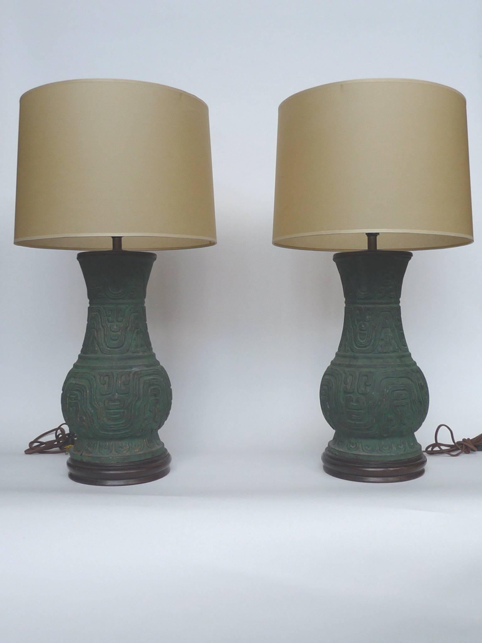 These two Chinese table lamps have bronze bodies capped with at the top and secured to a wooden base. The patina of the bronze is a gorgeous oxide green. These lamps are newly rewired and paired with new parchment shades with silk trimming. With a