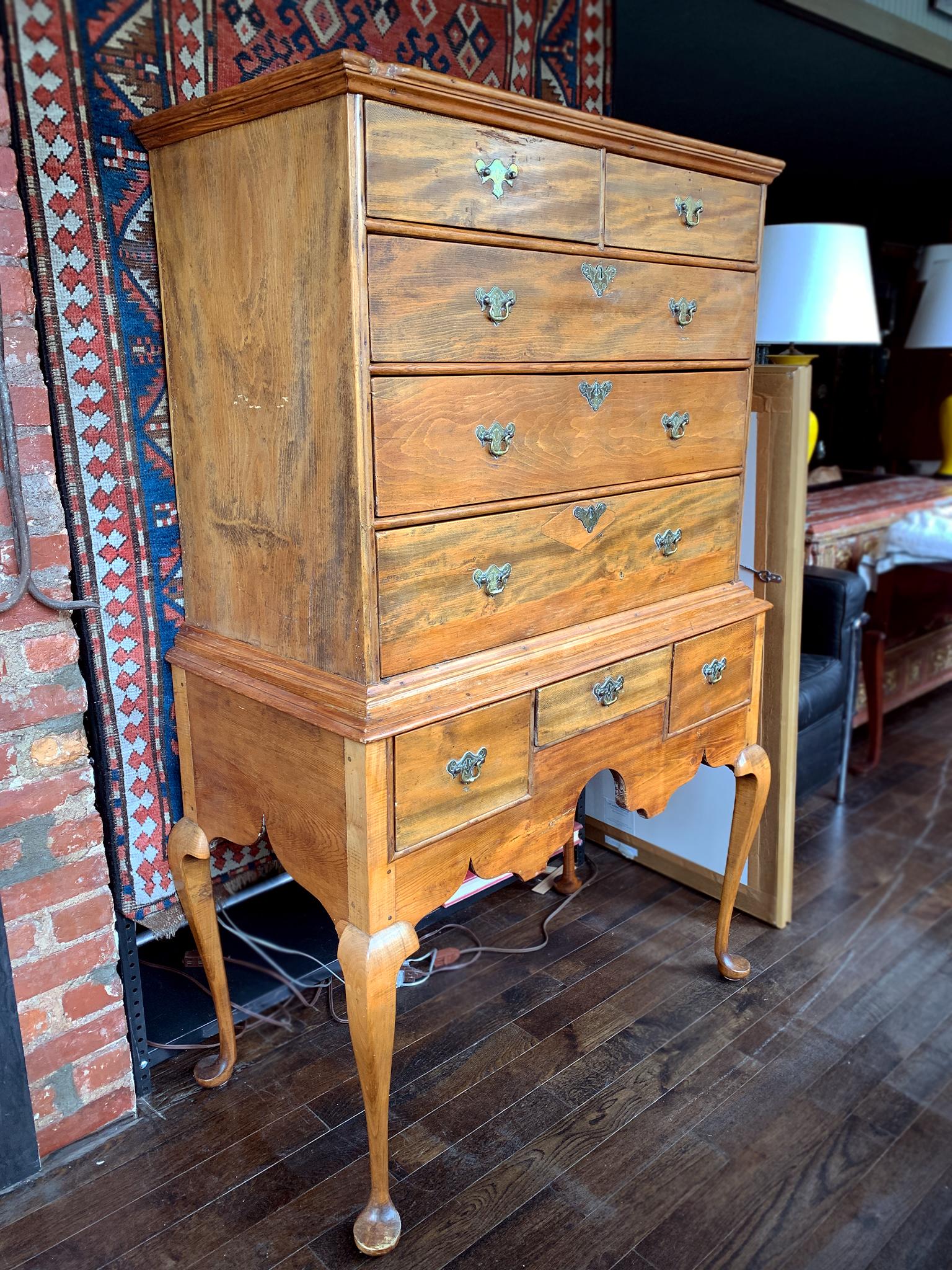 A classic Queen Anne highboy hand-crafted in America in 1750. It's comprised of pine and maple wood with a rich reddish brown finish. The woodwork is exquisite. Two cases make up the structure. The top segment is a flattop with 2 small drawers and 3