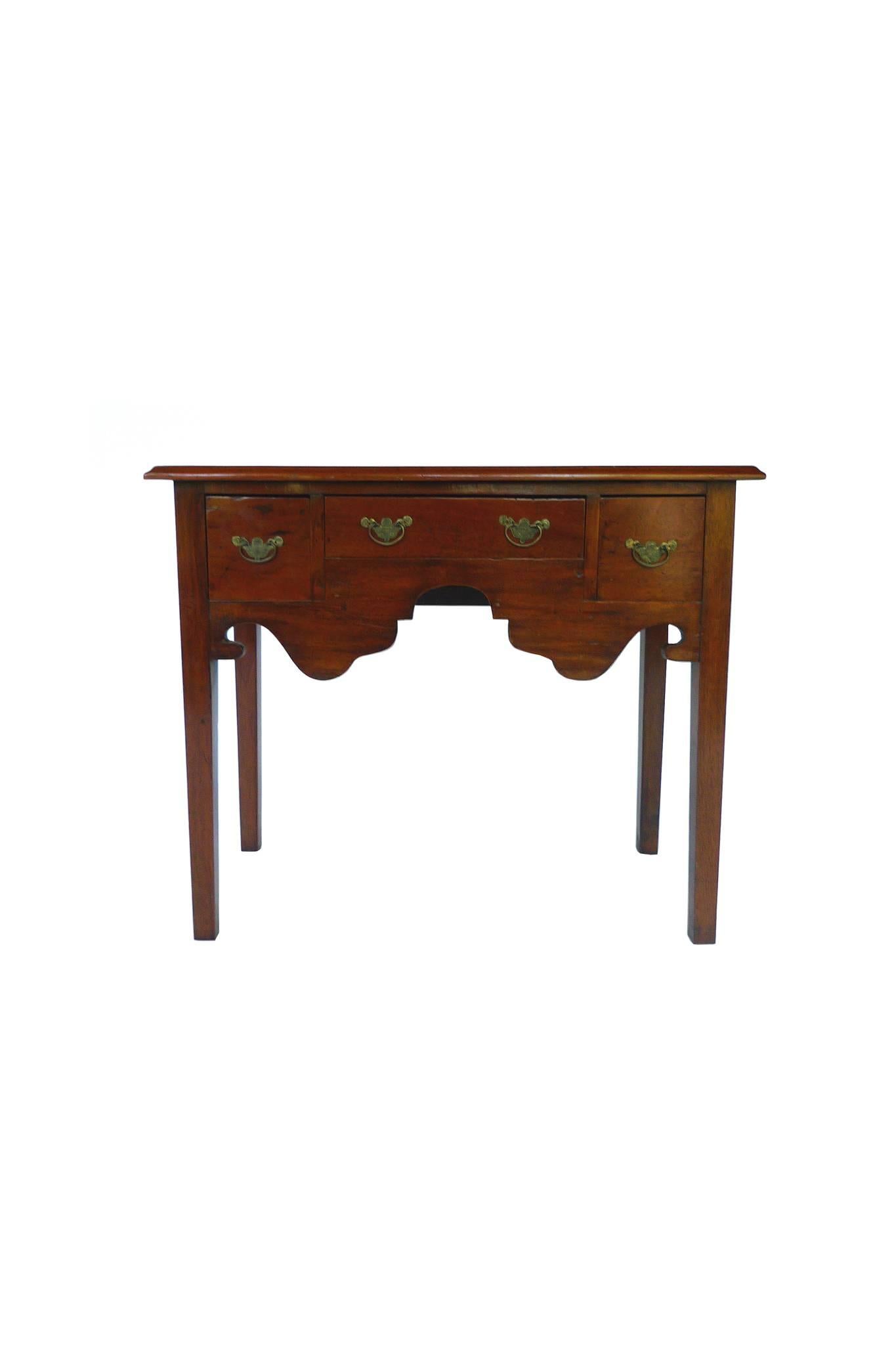 This 19th century lowboy or dressing table is newly refinished with a rich reddish-brown coat. The Chippendale-style design includes an apron with a central arch, straight tapering legs, and a flattop with an elegant molded edge. The three drawers