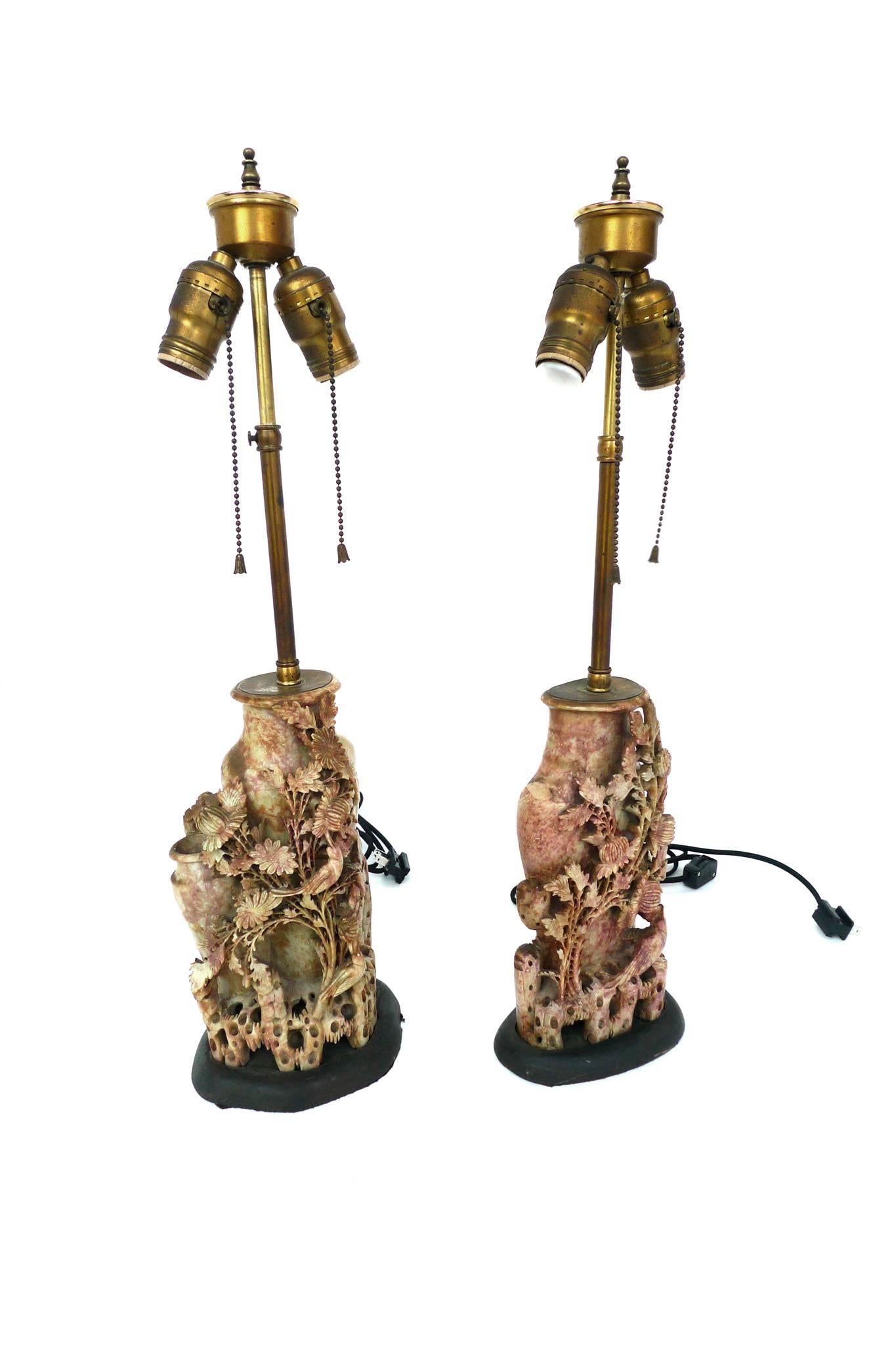 These are an exceptional pair of lamps. They are carved soapstone, richly textured in a rose tint. The carvings are an intricate floral design with bird figures. They are paired with new egg-white parchment shades in an oval taper. The lamps are