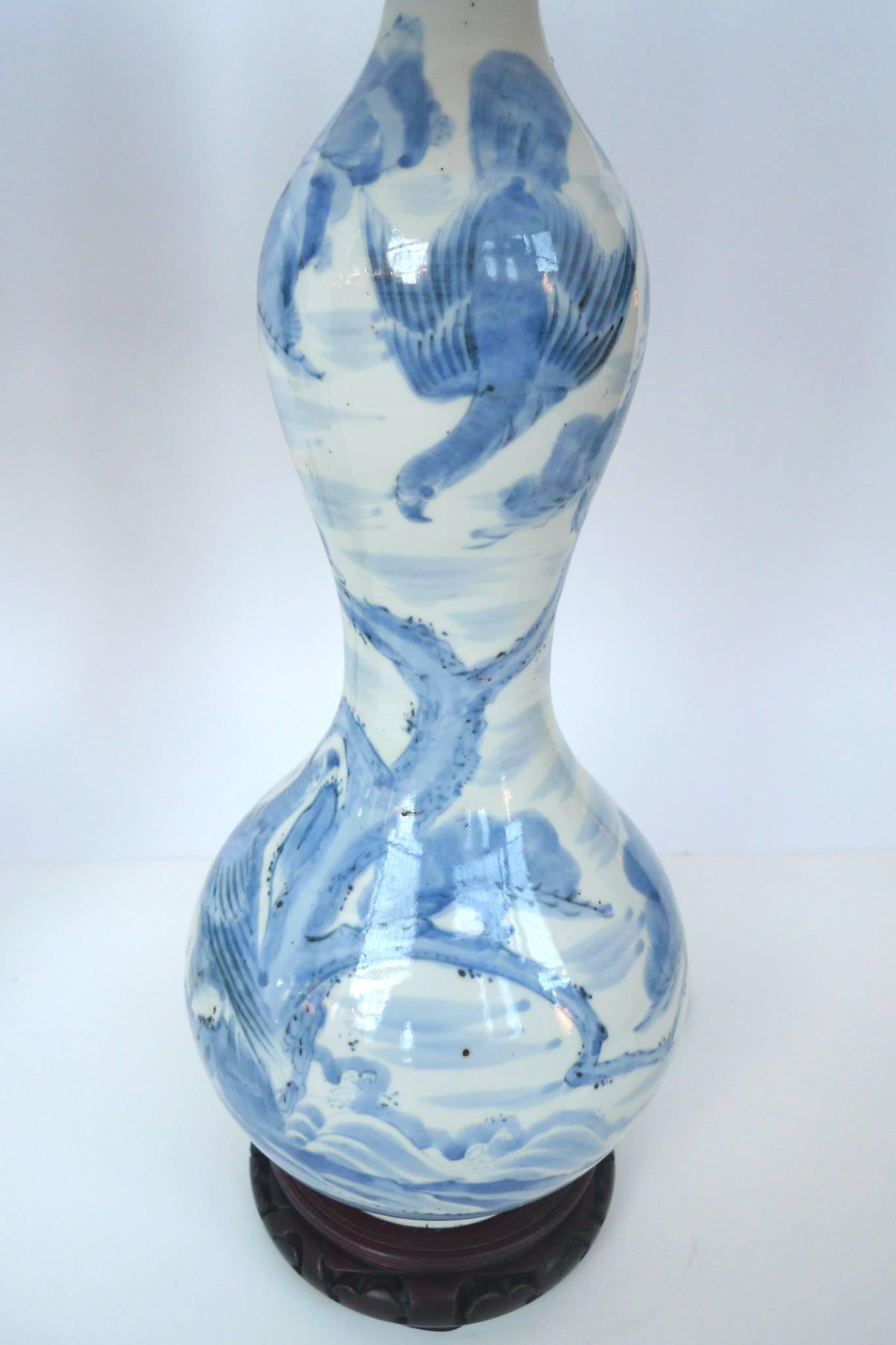 These gourd vase lamps are ceramic. They are paired with new silk-lined parchment shades in a round taper. The vases are beautifully hand-painted in a blue-and-white design of a pastoral landscape. While the vases are 19th century, the rosewood