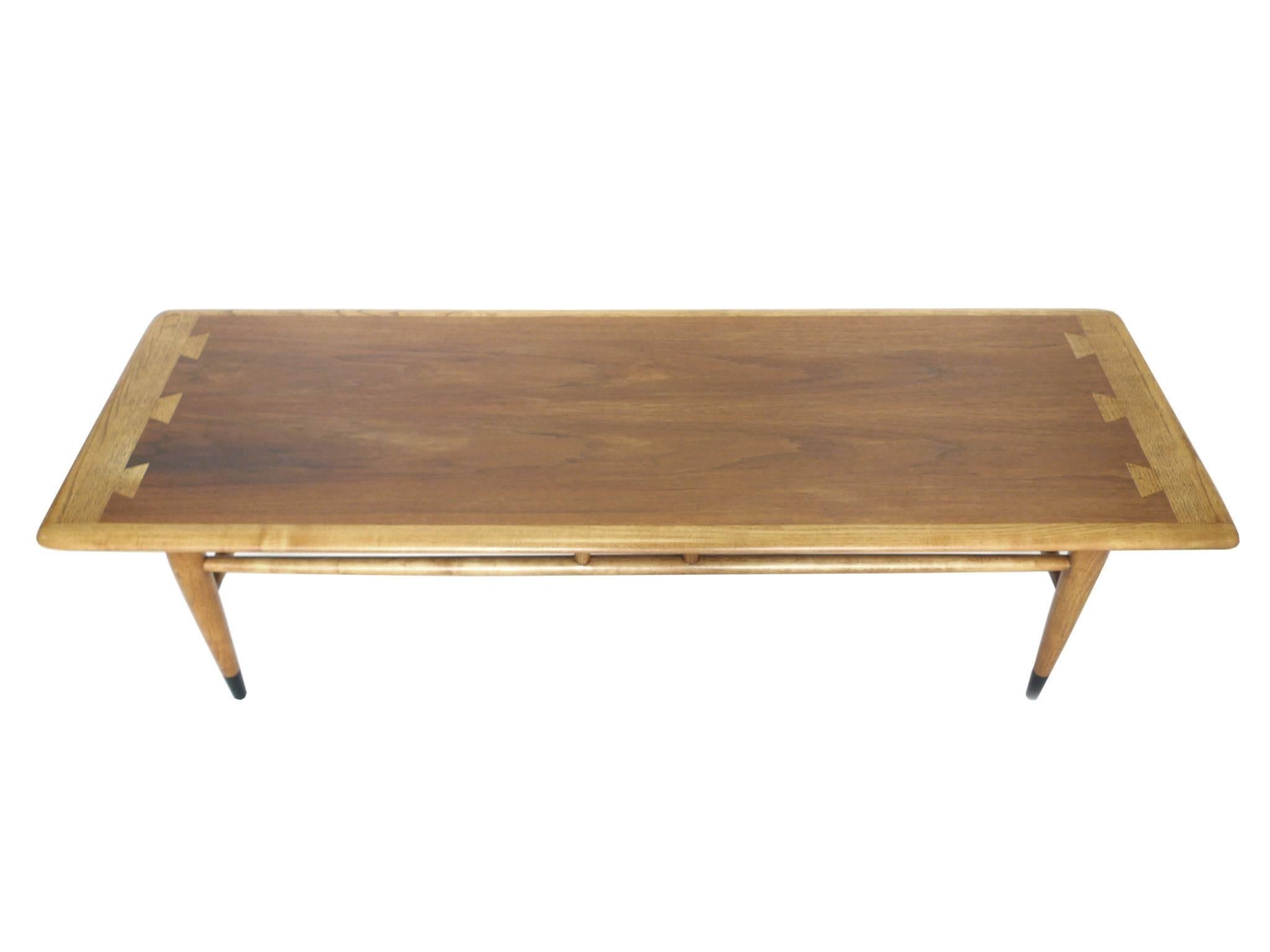 This Mid-Century coffee table manufactured by Lane Furniture is iconic for its two-toned wood top, pieced together with beautiful dovetail joints. This table is newly refinished, accentuating the rich grains of the wood. Other outstanding design