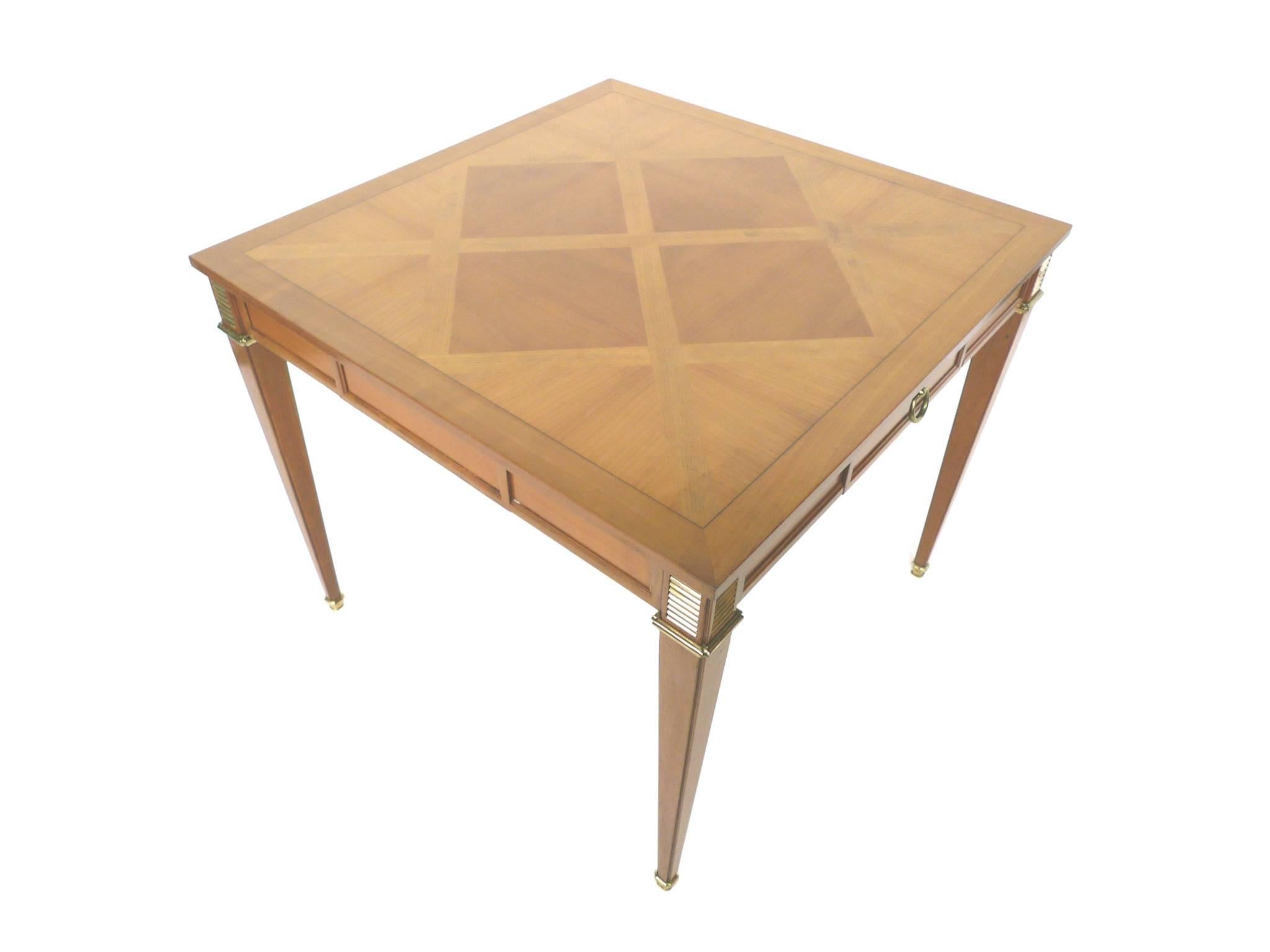 This Mid-20th century game table consists of mahogany wood with brass accents. It was manufactured by the Baker Furniture Company. Among its remarkable features are the parquetry pattern of the table-top, which is newly lacquered, the tapering legs,