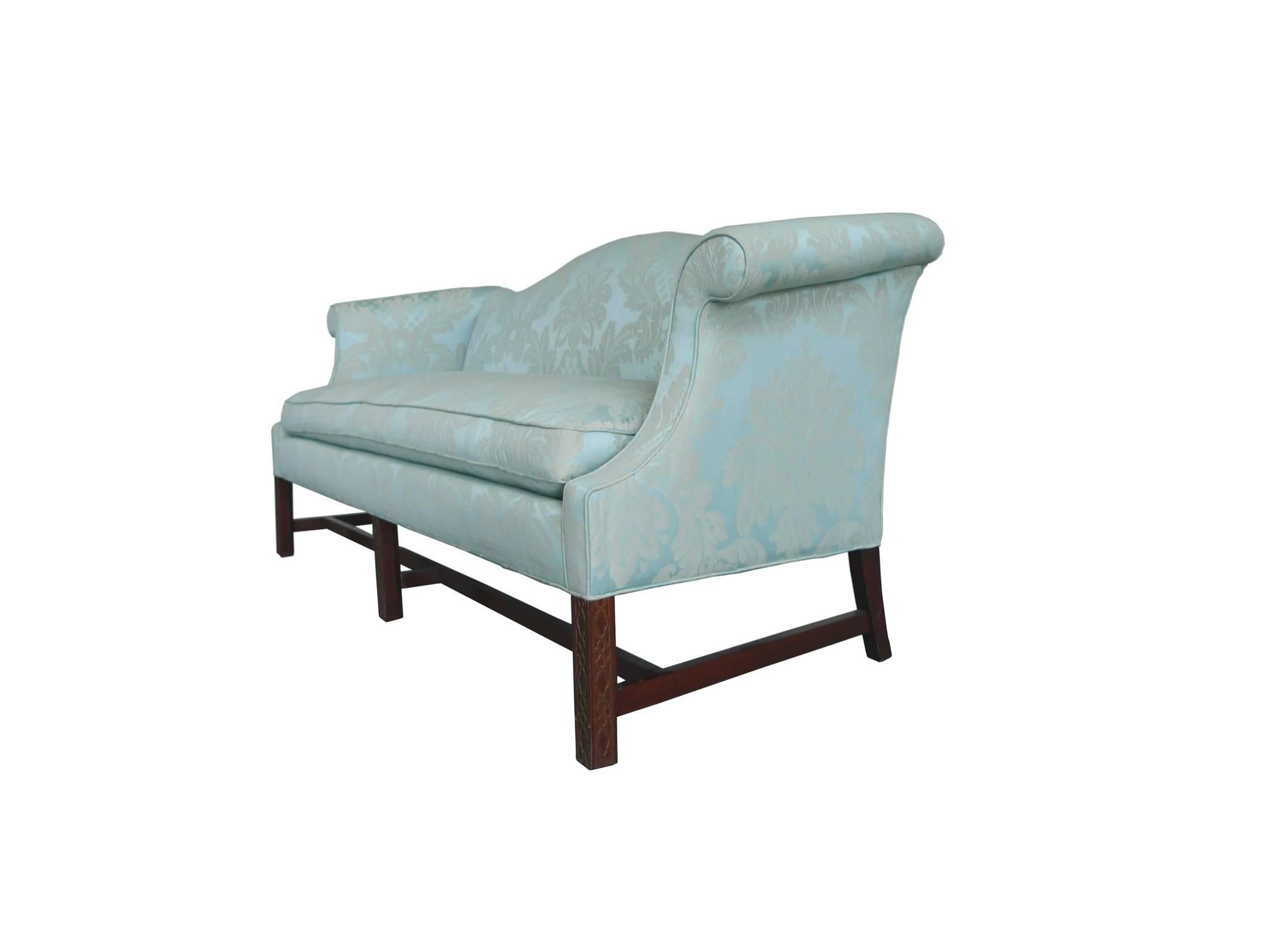 This 20th century sofa is in the Chinese Chippendale style. It's reupholstered in a stunning blue damask silk. The sofa's design includes a camelback, scrolled armrests, and soft edges with piping. The three front legs have a trellis design, while