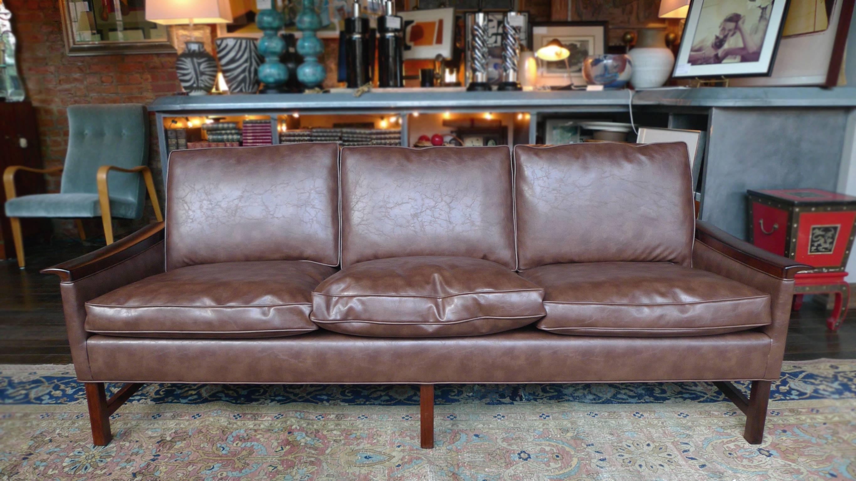 This Swedish sofa was designed and manufactured by Bröderna Anderssons. It's comprised of rosewood frame and legs that have been newly refinished. The sofa is reupholstered in a beautiful brown faux leather. The three-seat cushions are new as well.
