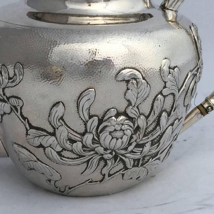A three-piece Chinese export silver tea set, circa 1900. The lightly hammered round bodies have been repousse worked with flowering chrysanthemums, that bloom through the Frost. The spout of the tea pot and the handles of the three pieces are worked