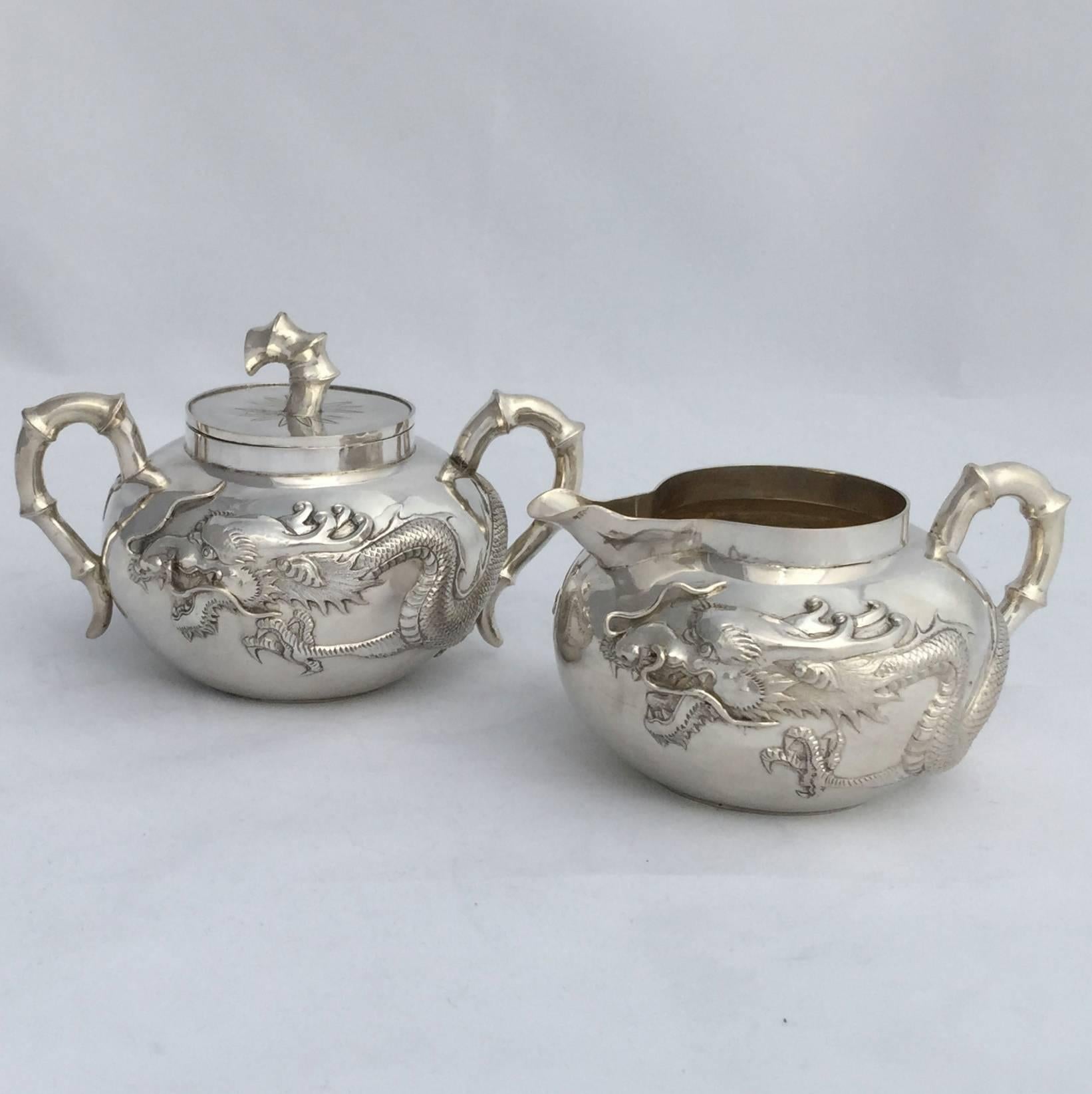 A Classic Chinese Export silver (CES) three-piece tea set. Each piece has been repousse worked with four clawed dragons against a polished surface. The sugar bowl retains its original lid and both the sugar and cream have gilded interiors. The