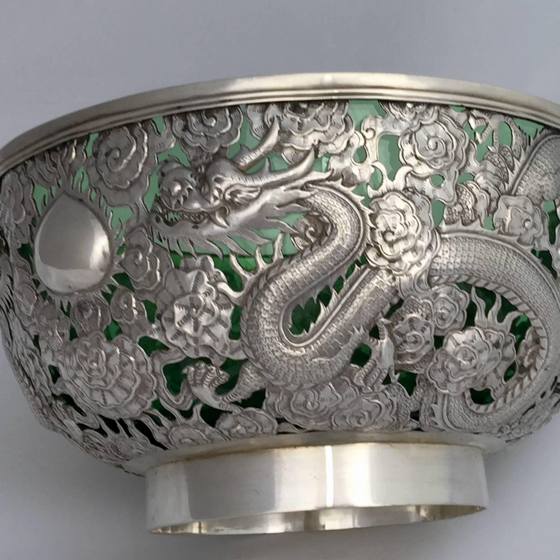 A large and finely worked Chinese export silver (CES) presentation bowl. The pierced and repousse worked body has four dragons cavorting in the clouds, including one breathing fire. Two dragons chase the magic pearl which forms a reserve for