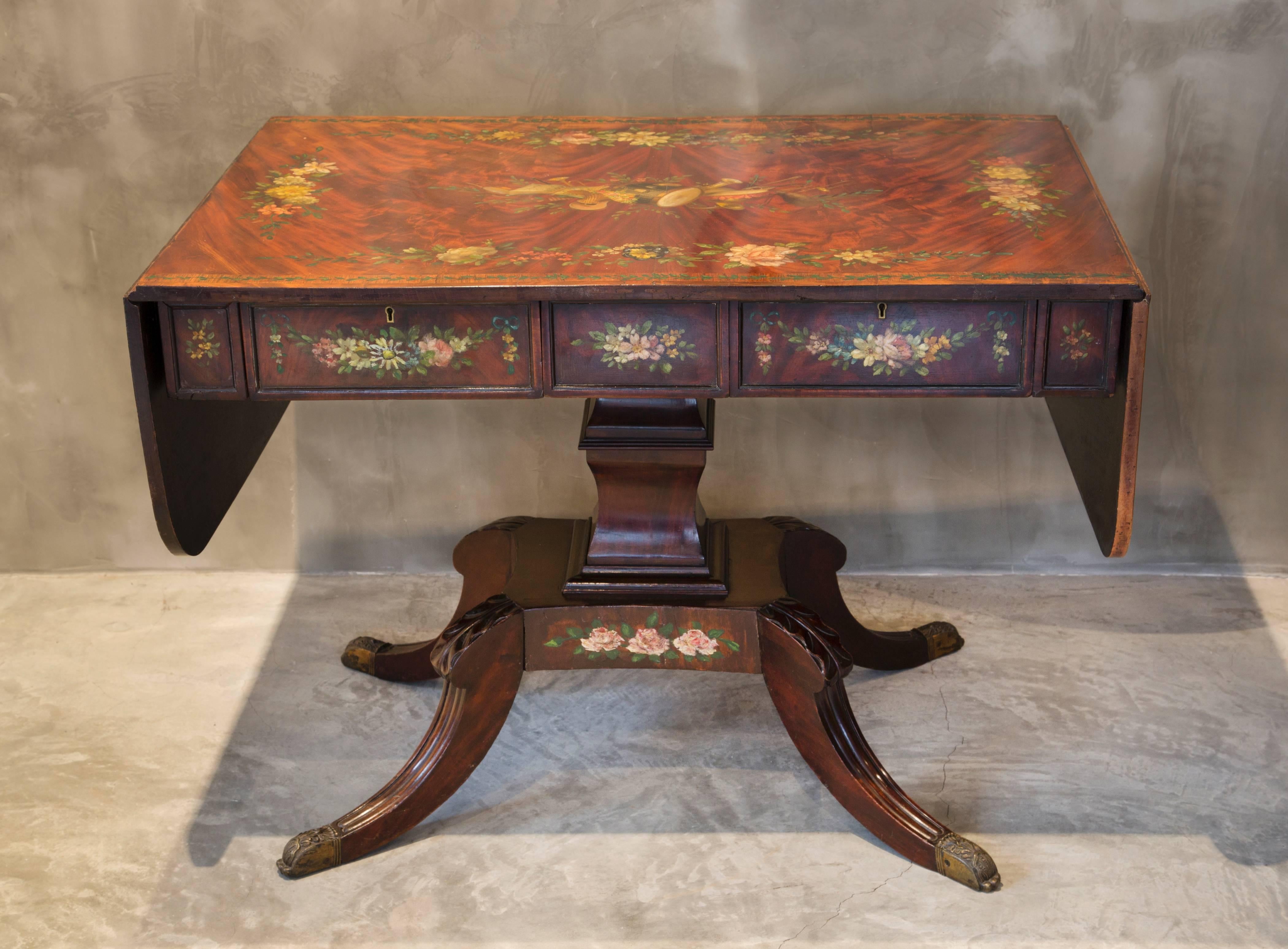 This beautiful Regency style burr mahogany table is a one-of-a-kind piece thanks to a previous owner painting it in flowers and musical motifs. It has handsome proportions with it's central column on sabre legs under two drawers, one stamped Edwards