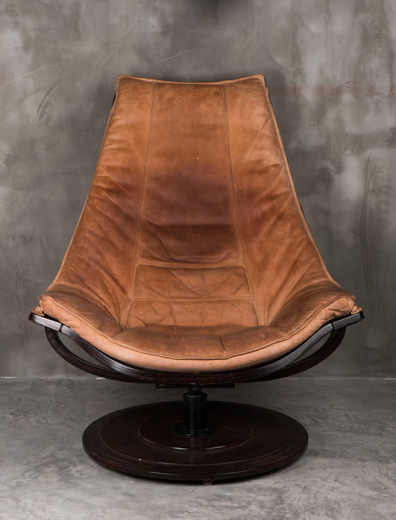 Uber cool tan leather swivel lounge chair by OM Designs Takashi Okamura and Erik Marquardsen, for NELO. Made in Sweden. 
Upholstered in tan leather. Stained, wooden beech frame on circular base. The swivel action is smooth, no problems. 
The