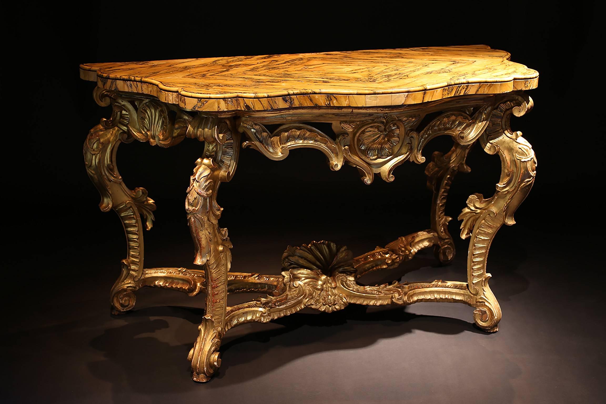 A mid-18th century Roman carved giltwood console table with a shaped serpentine Sienna marble veneered top with a shaped serpentine front and sides, standing on four legs joined by a stretcher base incorporating a carved shell. Good original