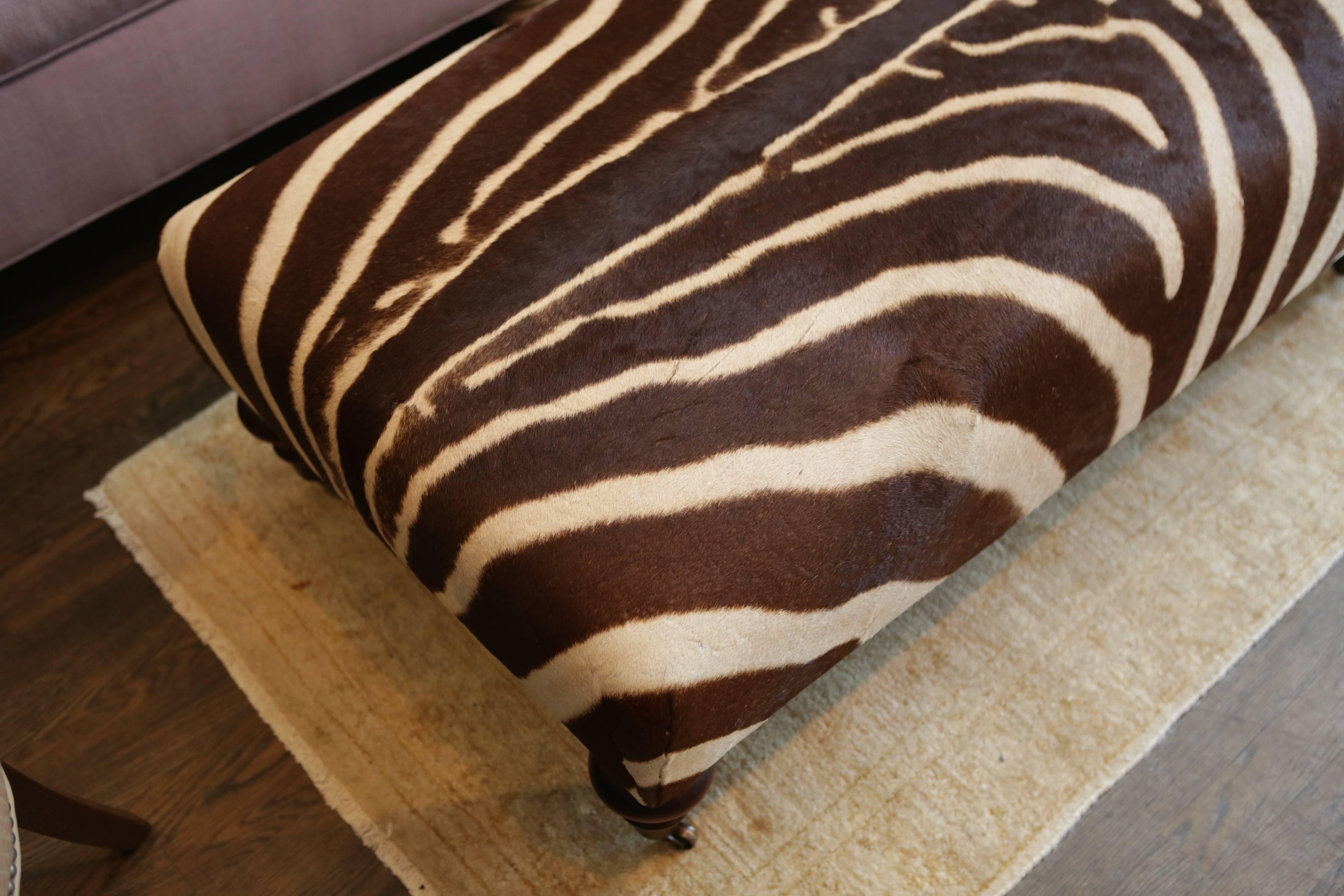 An authentic plains zebra hide upholstered ottoman with mahogany frame and casters.
