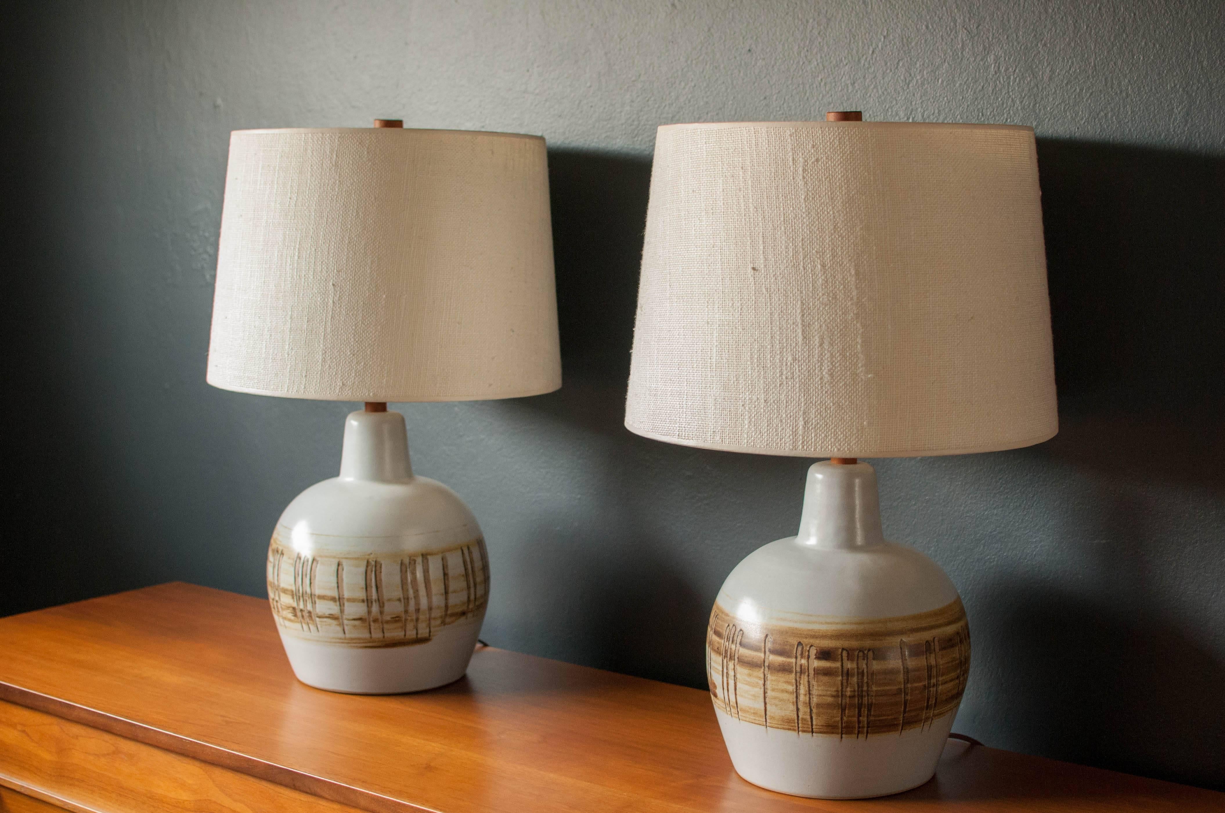 Mid-Century pair of pottery lamps designed by Jane and Gordon Martz for Marshall Studios. Stoneware white ceramic base displays a neutral tone finish complete with their signature walnut stem and finial. Price is for the pair. 

