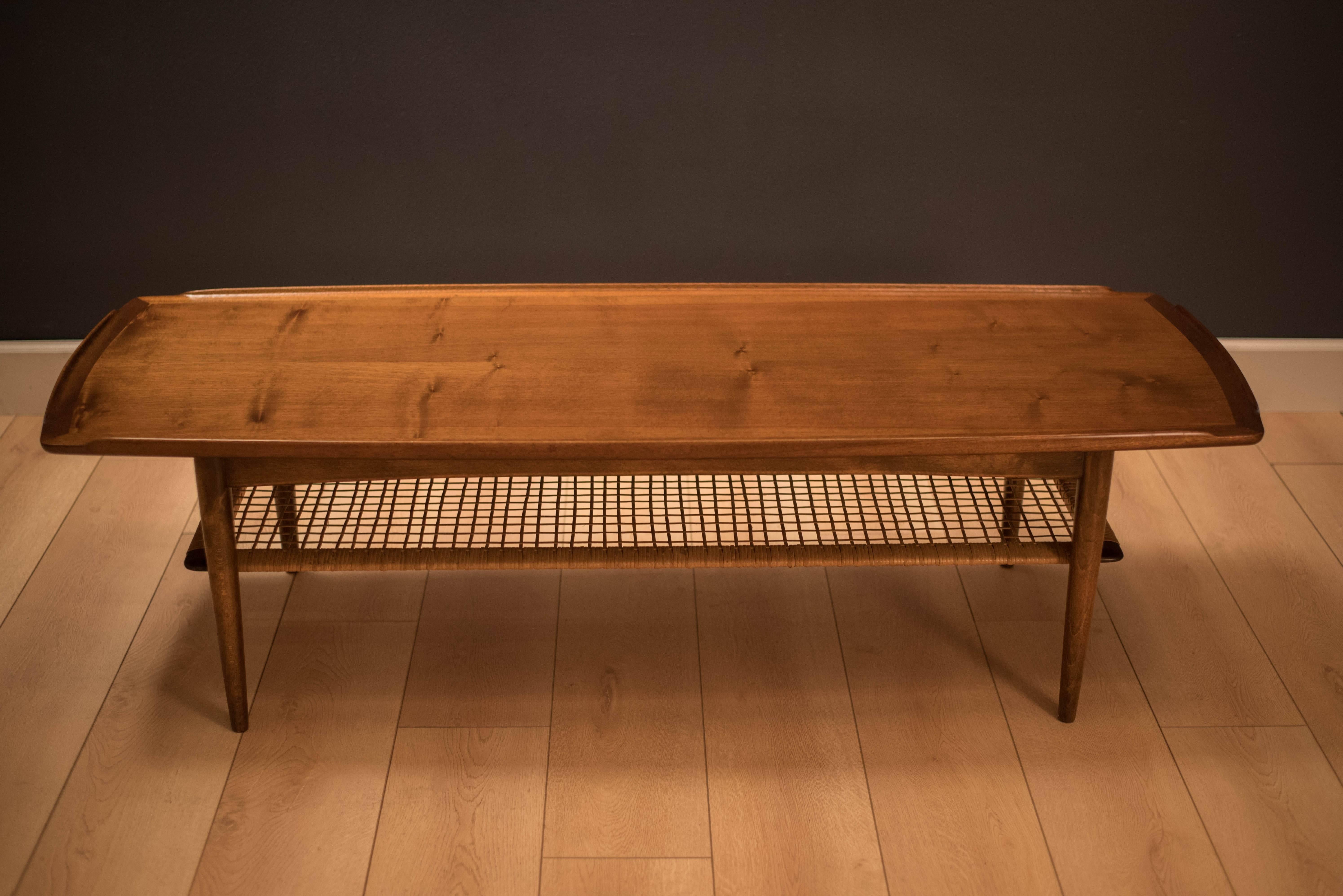 Danish modern coffee table designed by Poul Jensen for Selig. This piece is made of walnut and displays sculpted raised edges with a two-tier magazine shelf made of cane. 

.