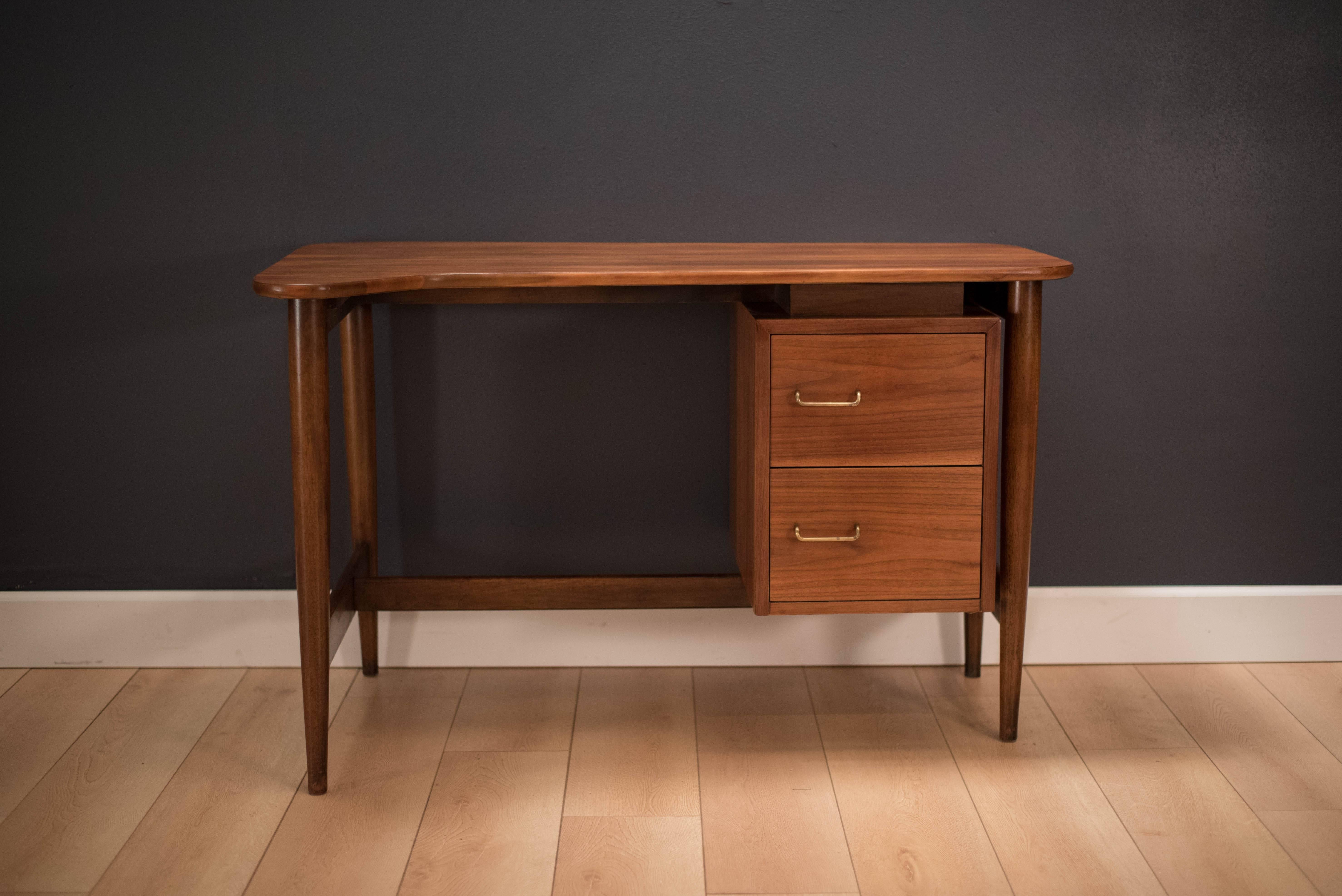 Mid-Century Modern Desk by American of Martinsville in walnut. This piece is from the Dania collection designed by Merton Gershun. Features two drawers with brass handles and a unique boomerang shaped top. 

