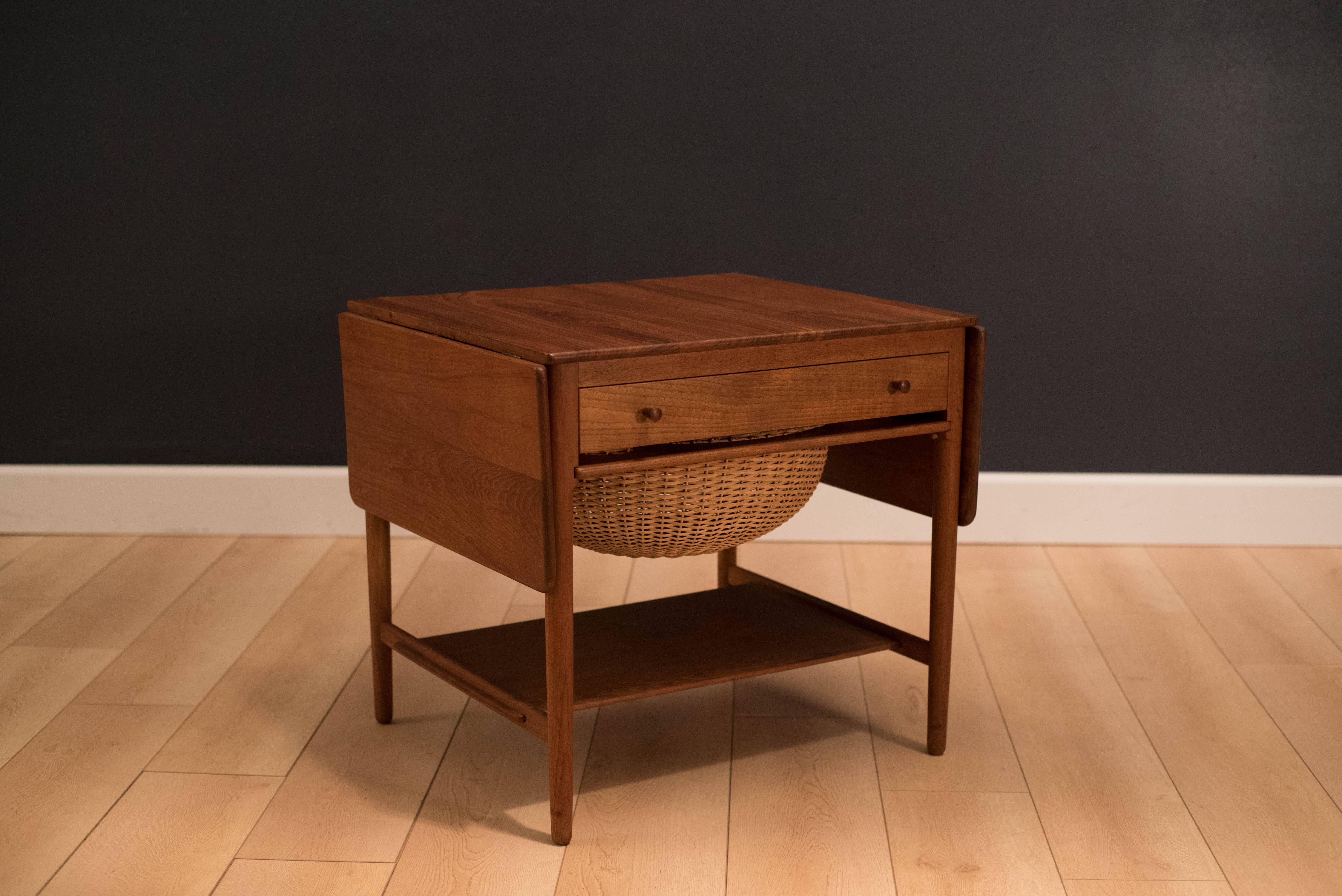 Mid-Century Danish sewing table designed by Hans Wegner for Andreas Tuck. This piece is constructed of solid teak and oak and features an extendable drop-leaf tabletop. Includes one drawer and pull-out wicker basket tray. Tabletop extends out to