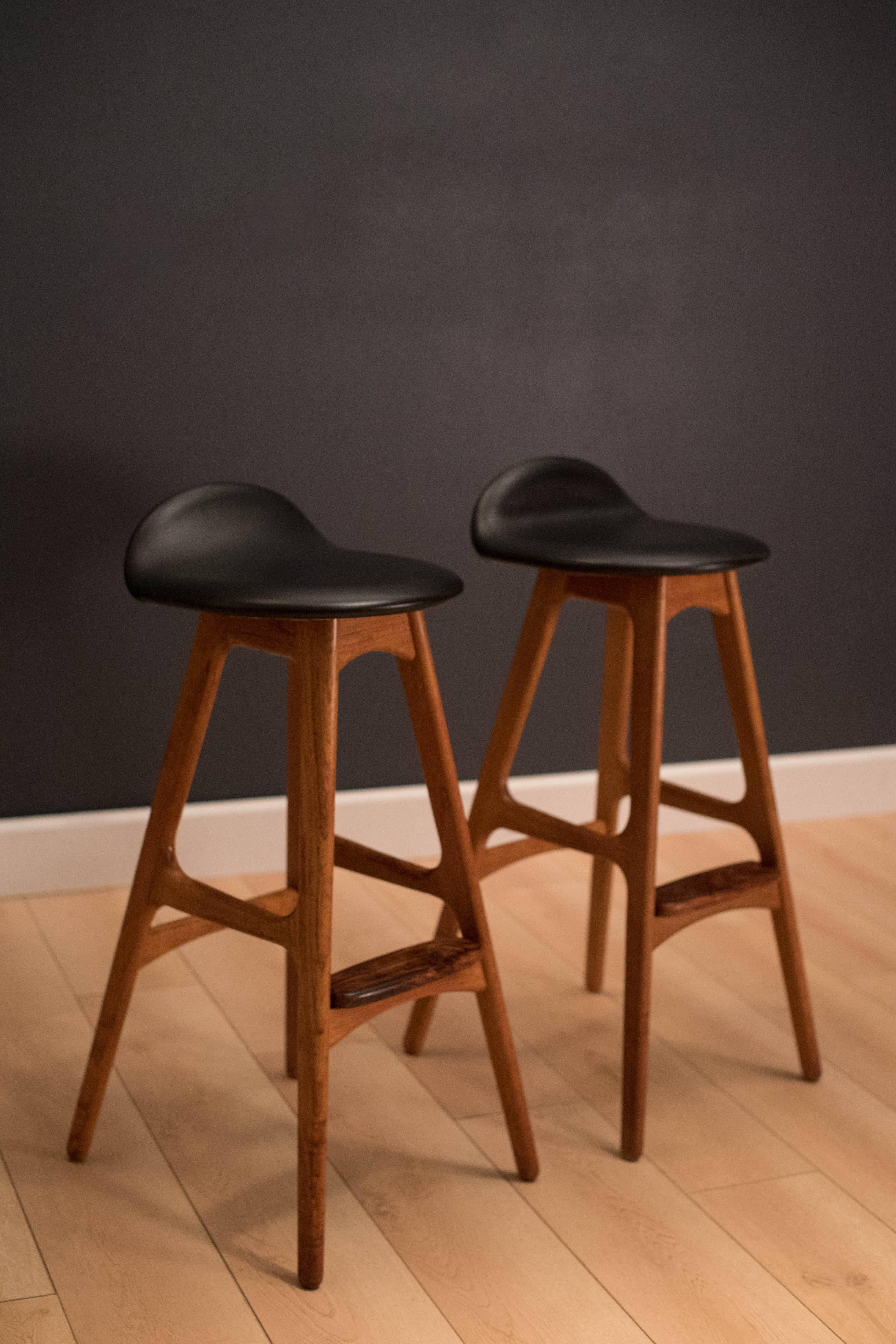 Mid-Century pair of bar stools designed by Erik Buch for O.D. Mobler in teak. This pair features the original black Naugahyde sculpted seats and attached rosewood footstool. 

