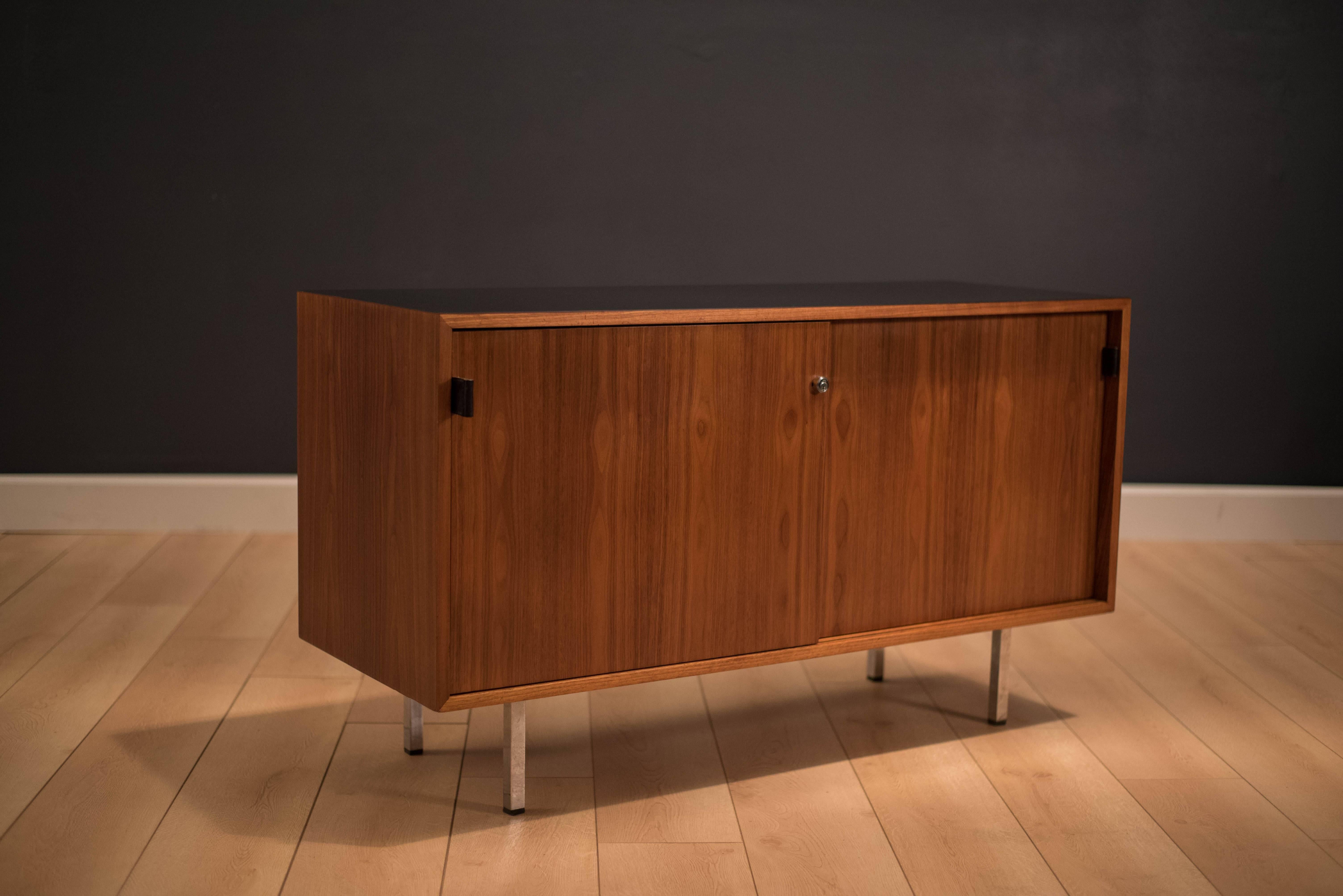 Mid-Century walnut credenza designed by Florence Knoll. This piece features a black formica top and is accessorized with black leather pulls. The interior displays adjustable shelving. 

 
