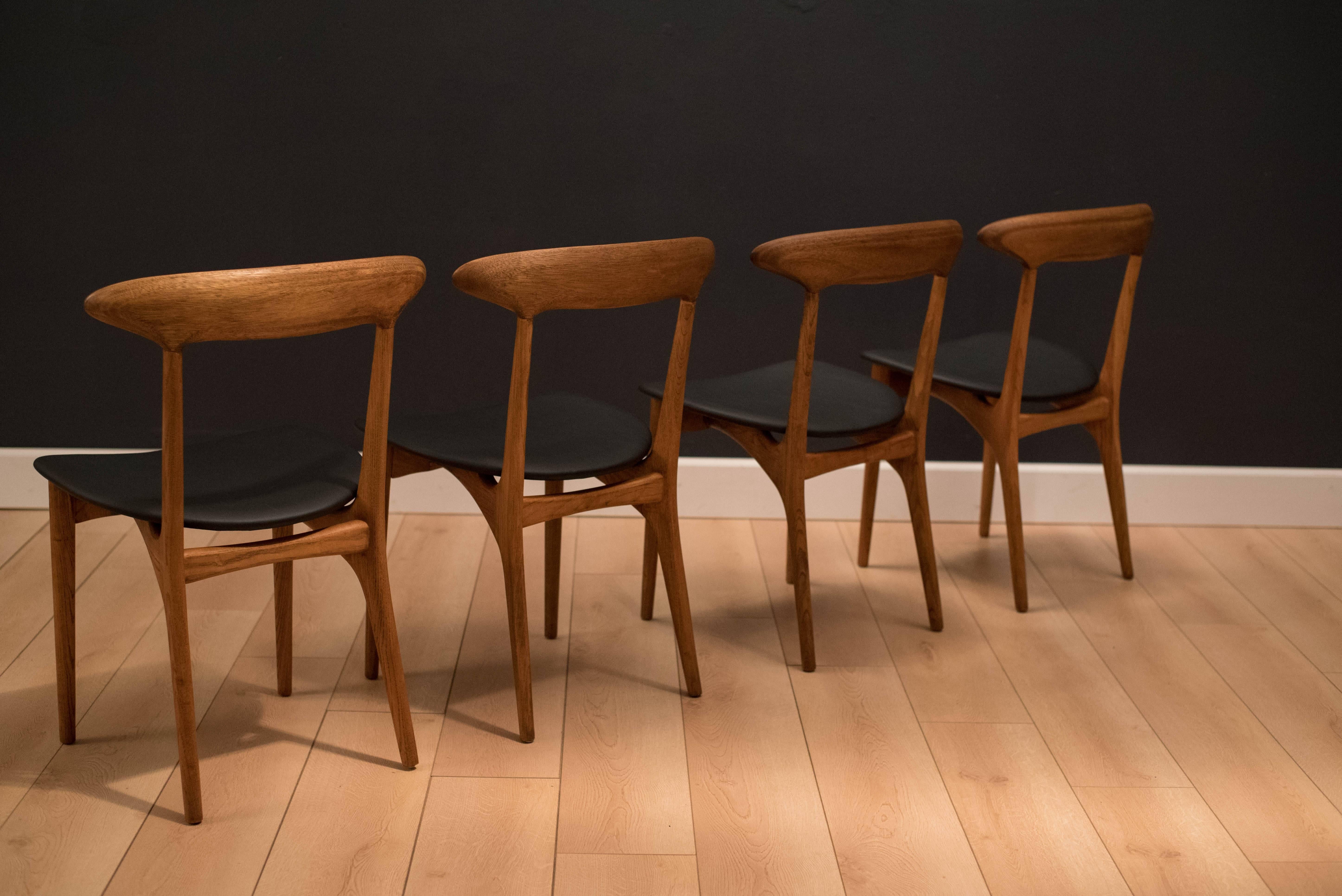 Mid Century set of four dining chairs designed by Kurt Ostervig. This set features sculpted backrests and nicely aged oak grains. Seats have been newly reupholstered in black vinyl. Price is for the set of four. 

 
