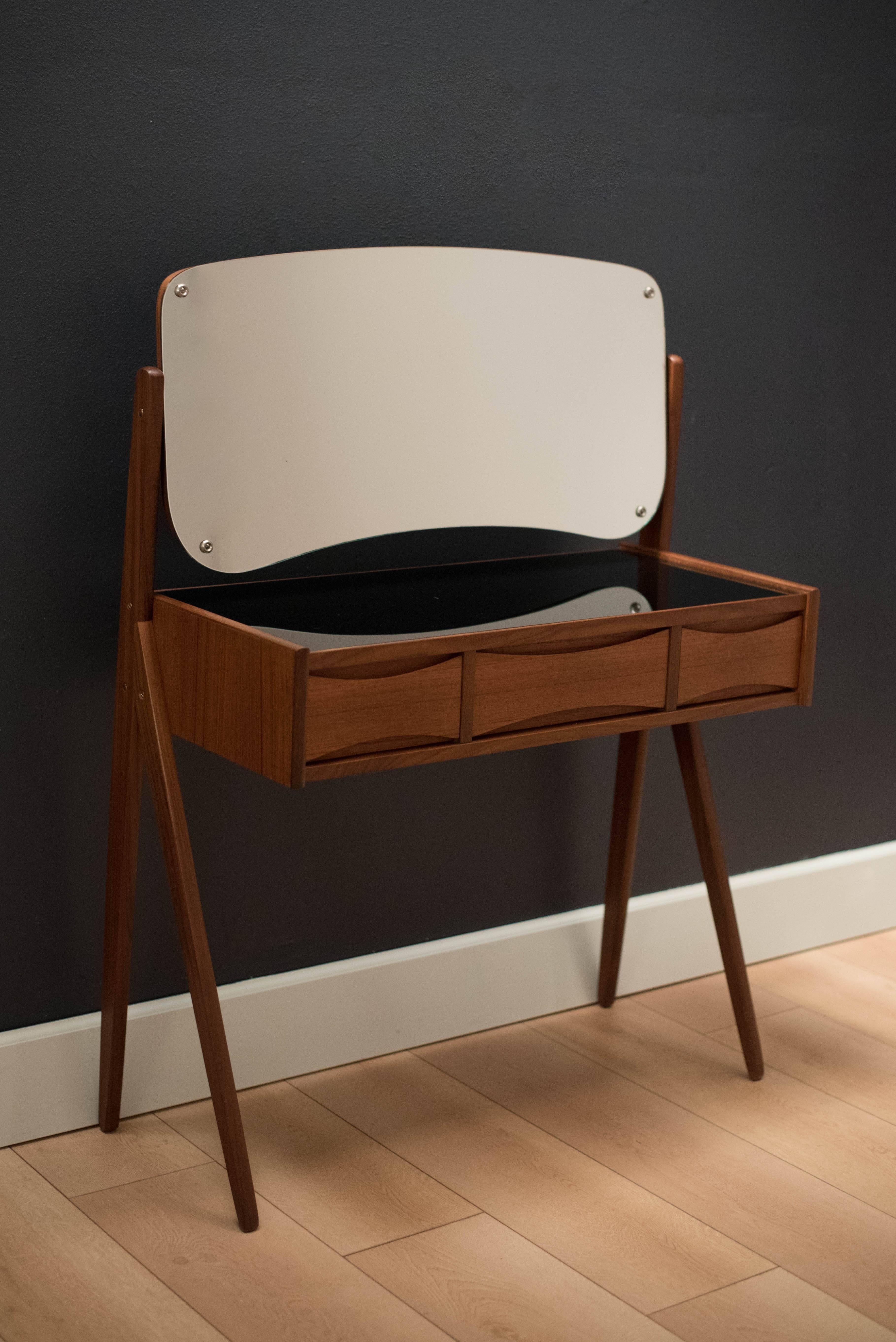 Danish floating vanity dresser table designed by Arne Vodder in teak. This piece showcases beautifully with it's unique external splayed legs. Includes three dovetailed drawers with signature sculpted pulls. Easy to maintain with a black plexiglass