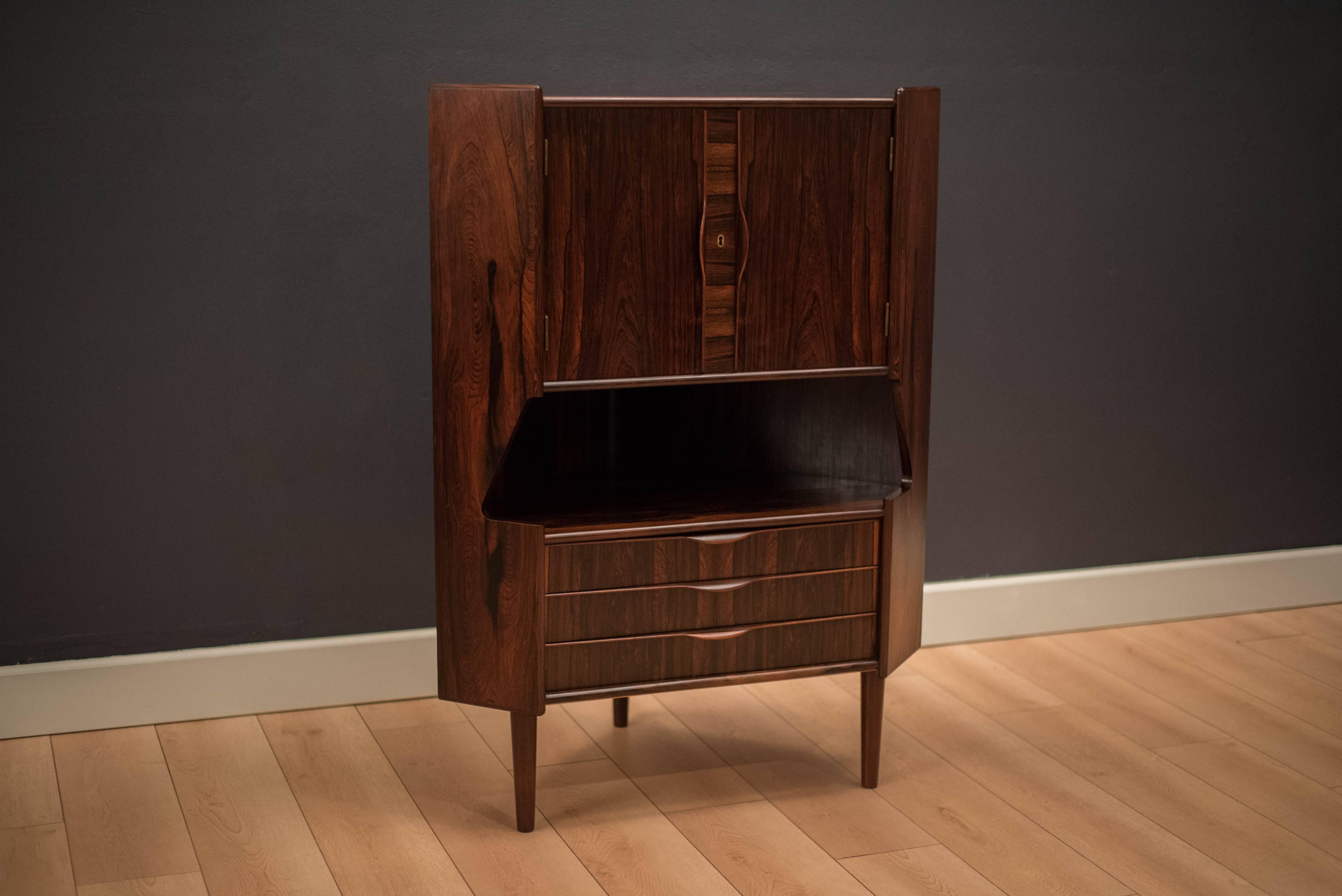 Mid-Century rosewood corner bar cabinet designed by Gunni Omann. This piece features three sculpted drawers with two doors that reveal open bar storage. Perfect solution for small spaces. Includes skeleton key.

Measures: 24.5