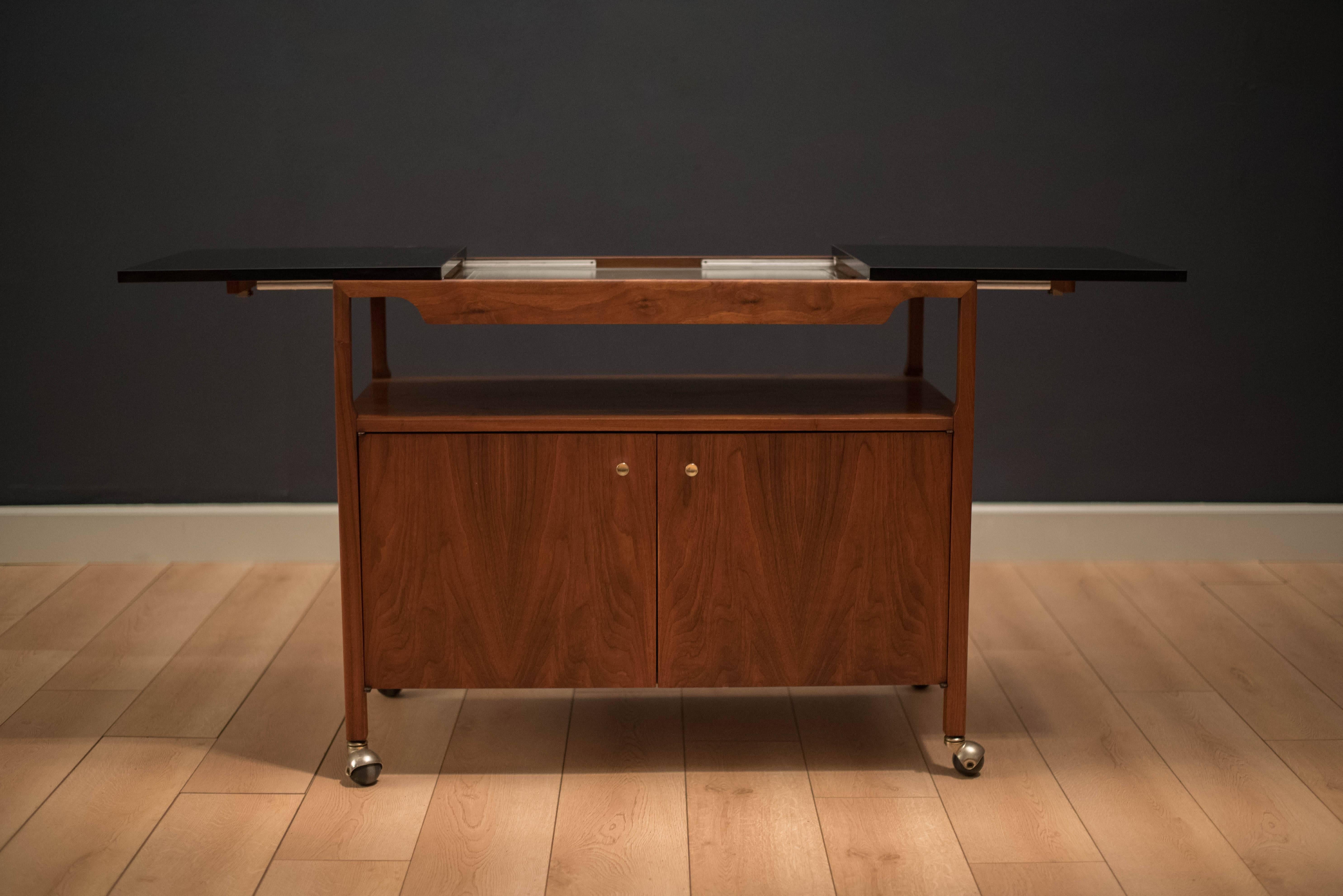 Midcentury serving bar cart by Brown Saltman in walnut. This piece displays a black Formica top that expands to reveal a warming tray. An open storage cabinet is provided below and the top of it can be used as a middle shelf.

Dimensions: 63" W