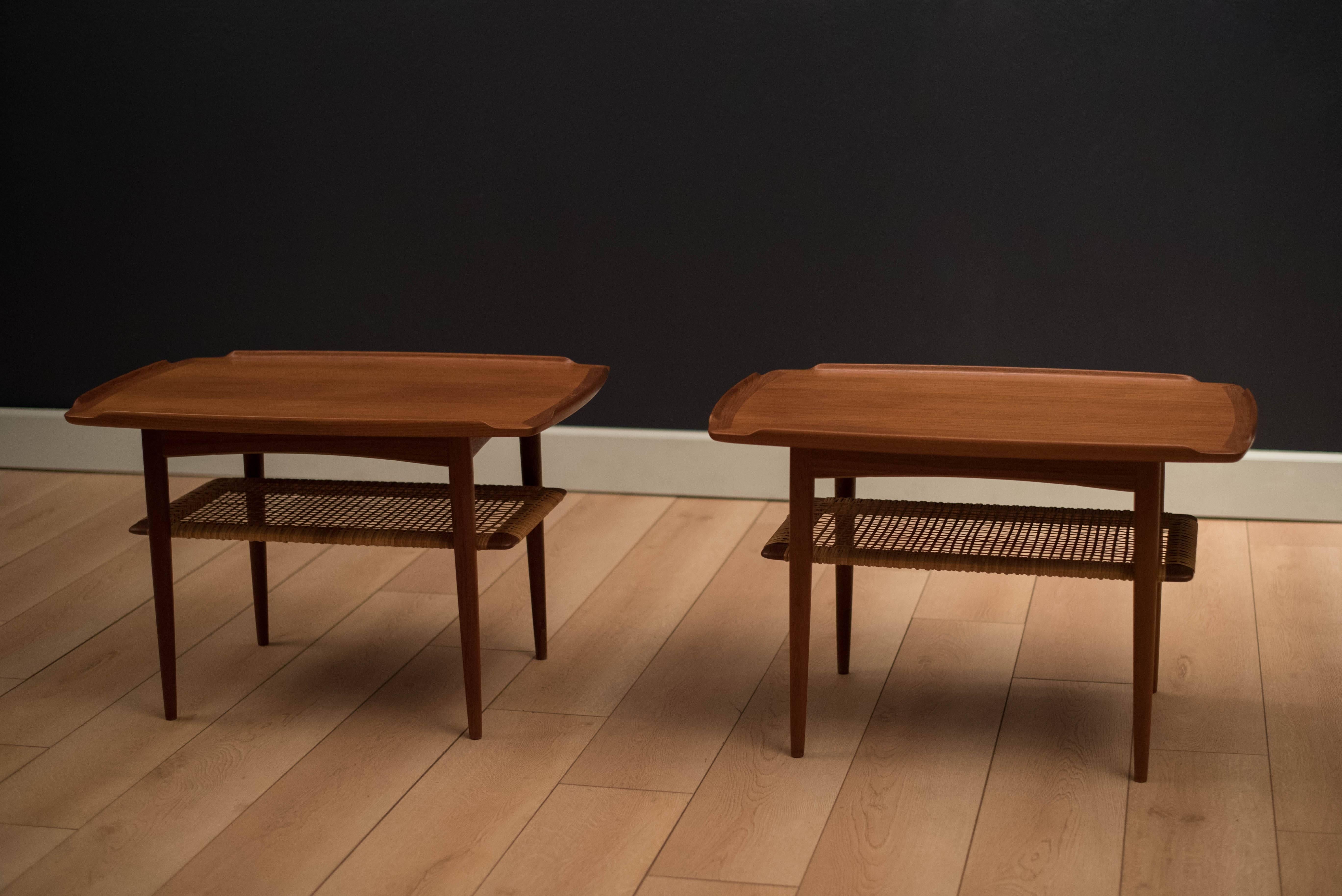 Danish pair of side tables designed by Poul Jensen for Selig in teak. This set features sculpted raised edges with a two-tier magazine shelf made of cane. Price is for the pair. 

  