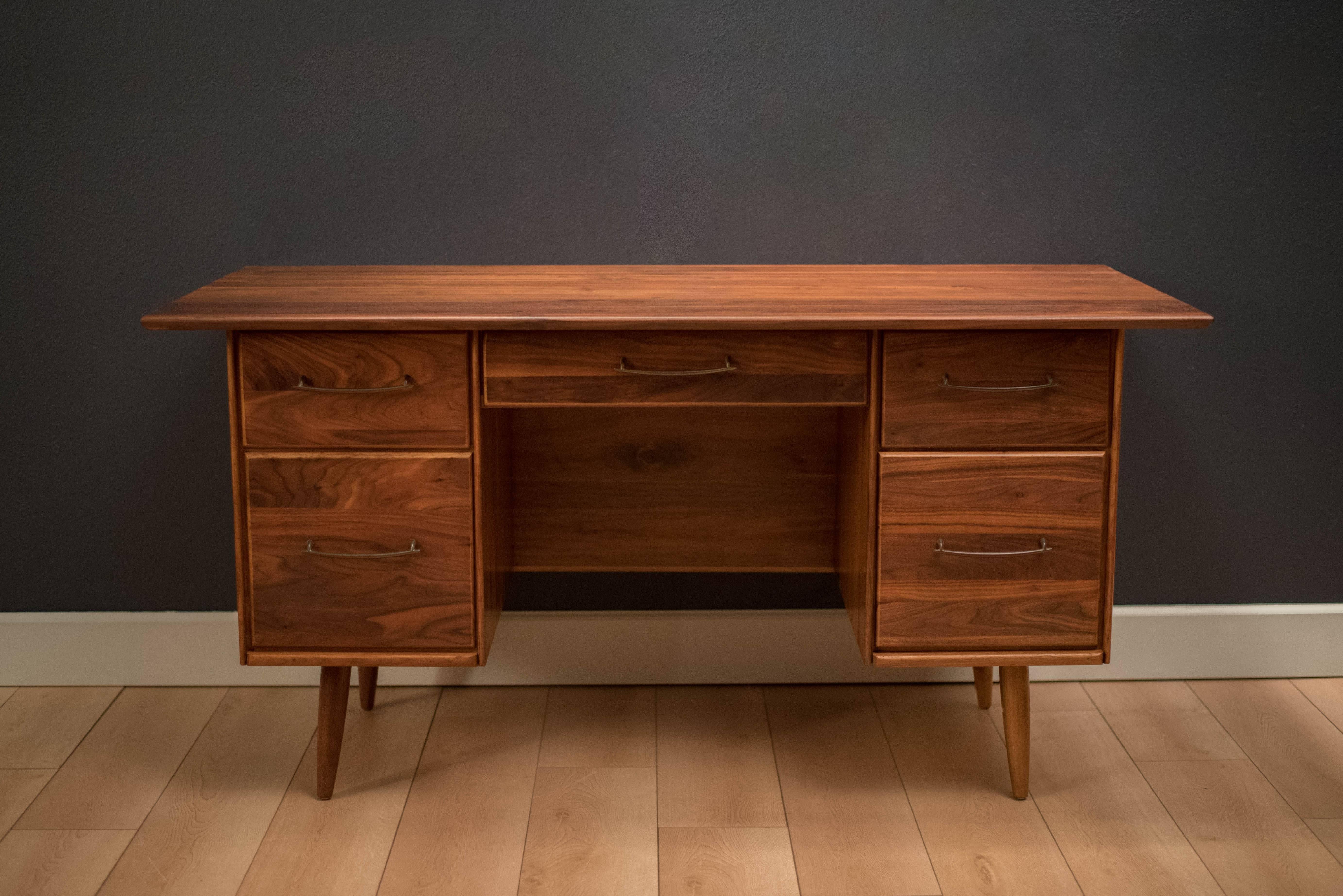 Mid-Century Ace-Hi executive desk in solid walnut. This desk offers plenty of storage space complete with five spacious drawers accessorized with pewter handles. Displays well from any angle and is finished on the back. 
 

 