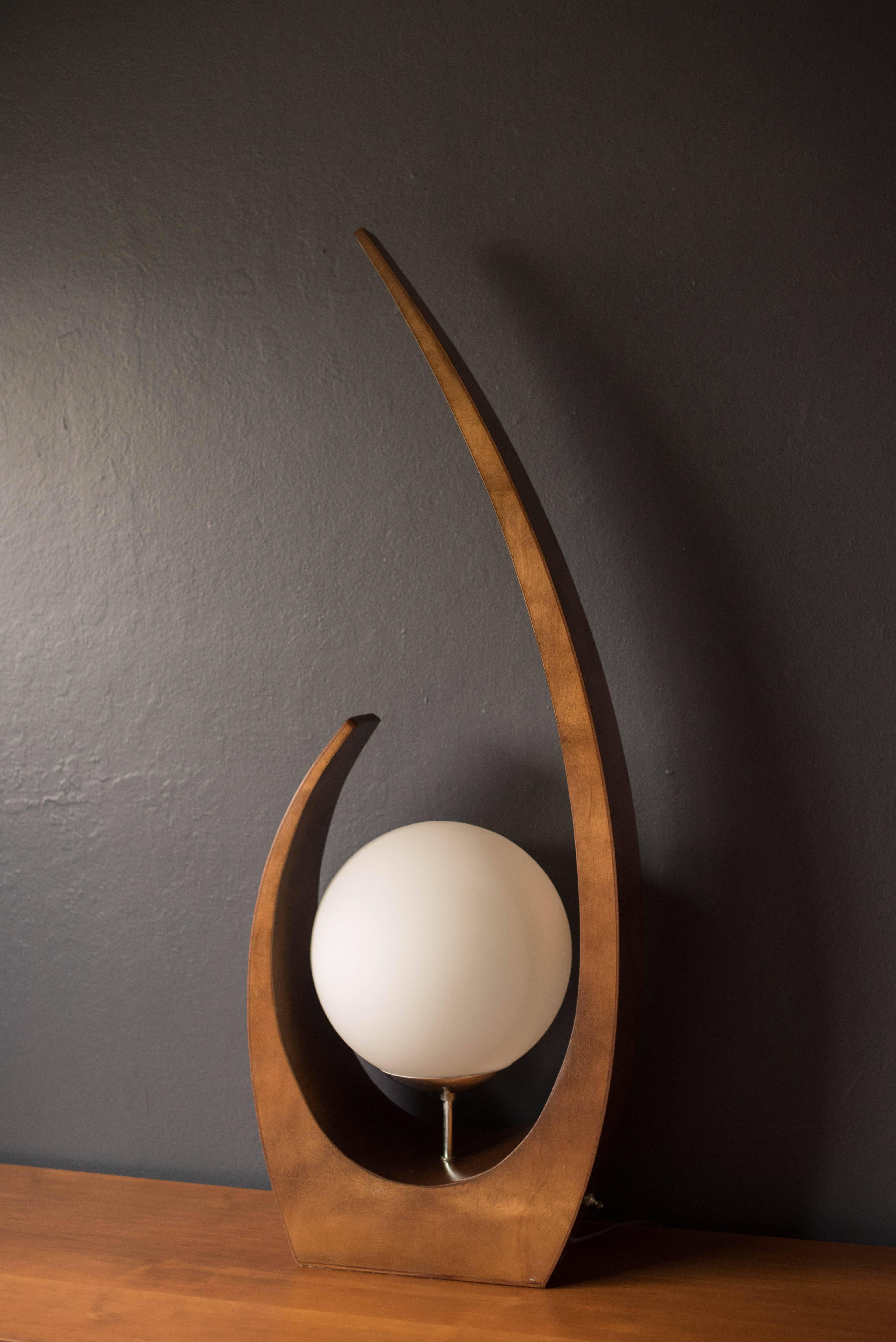 Midcentury sculptural lamp by Modeline, circa 1960s. This piece features a white frosted glass globe with bent plywood base. Includes a three way switch. 



 