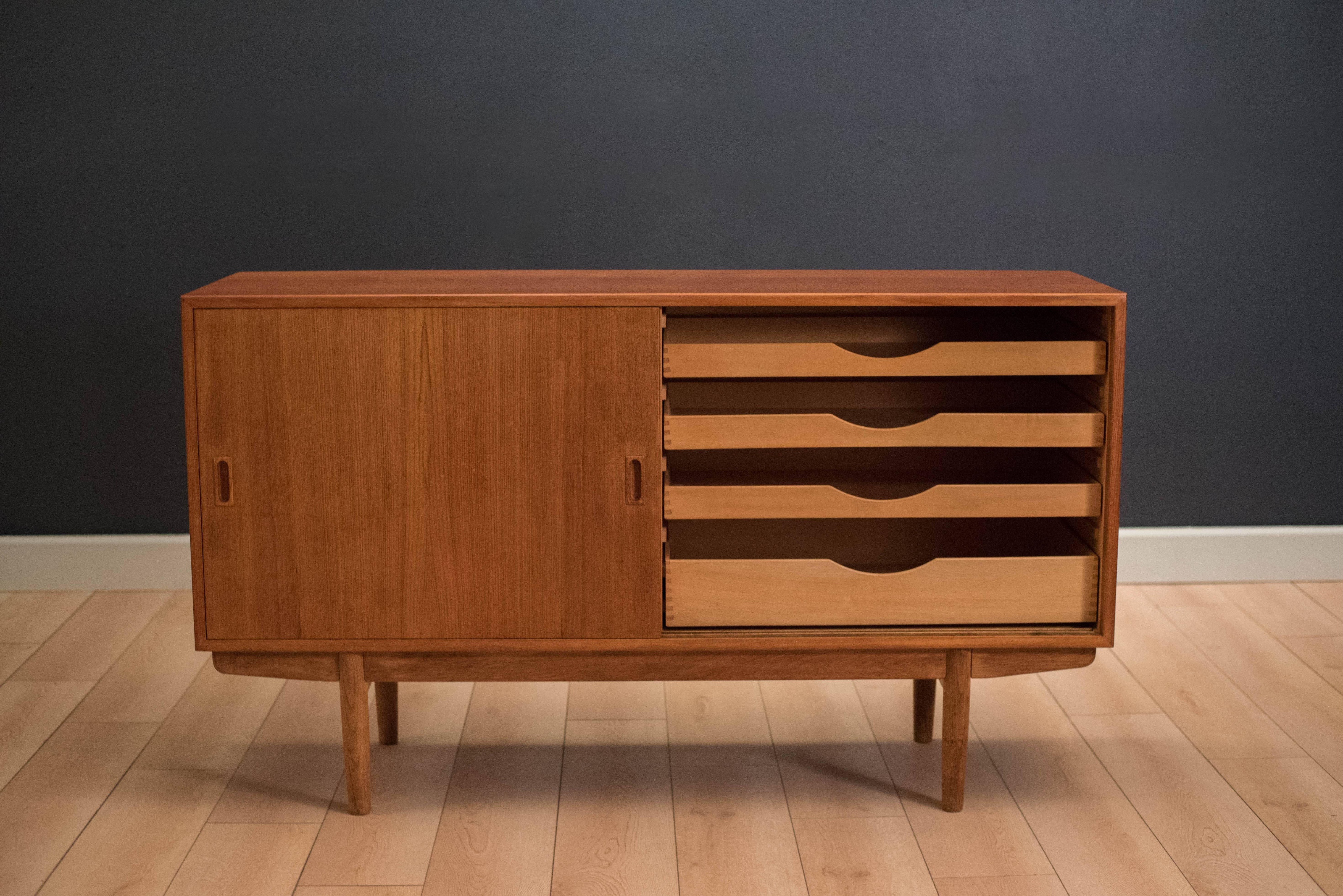 Danish sideboard designed by Borge Mogensen in teak and oak. This piece features sliding doors that glide on wood rails accessorized by sculpted handles. Includes four dovetailed drawers and two adjustable shelves. 

 