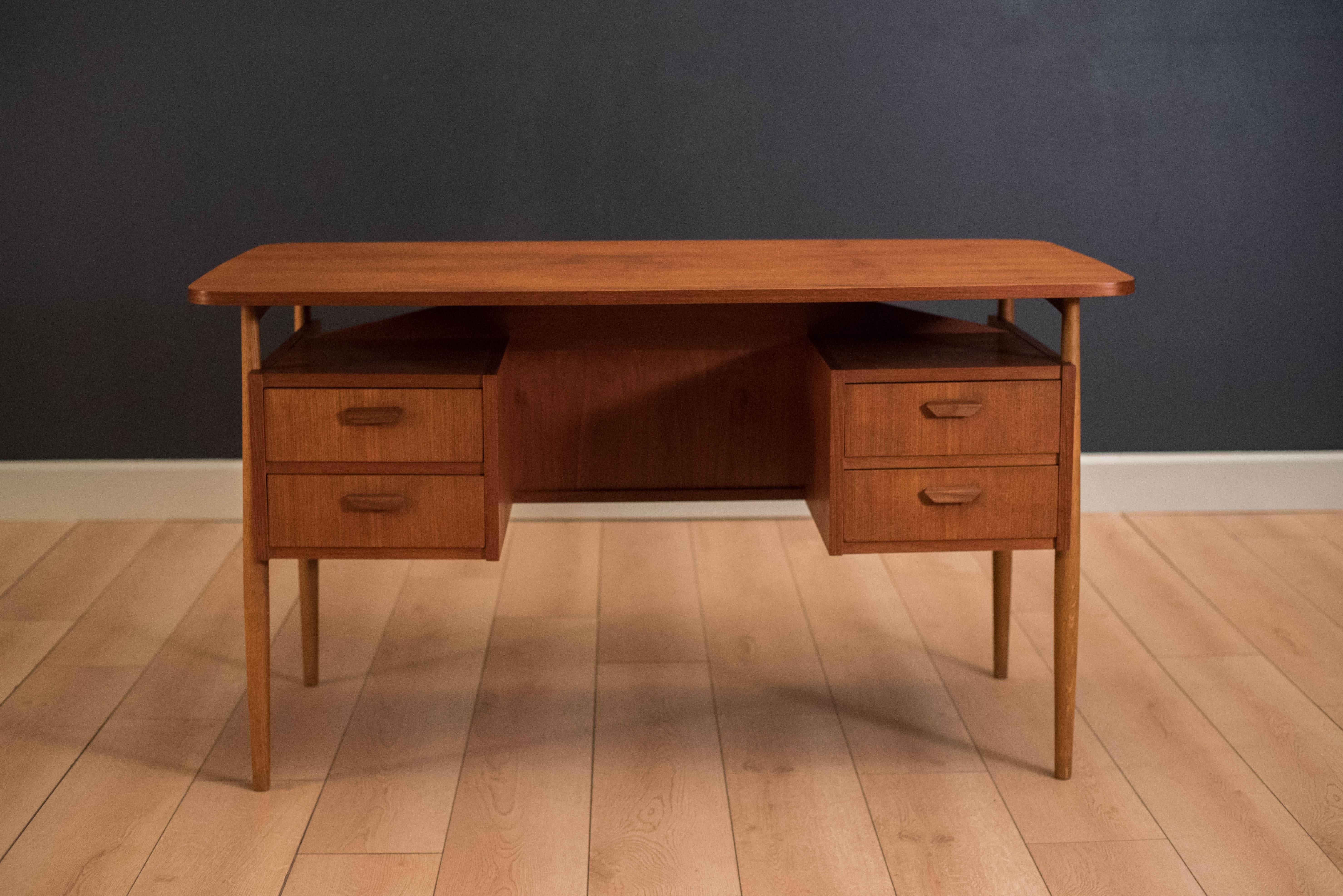 Mid-Century desk by Gunnar Nielsen Tibergaard in teak. This piece features a floating desk top with external oak legs. Includes four dovetailed drawers and an open bookshelf storage which can be displayed from any angle.