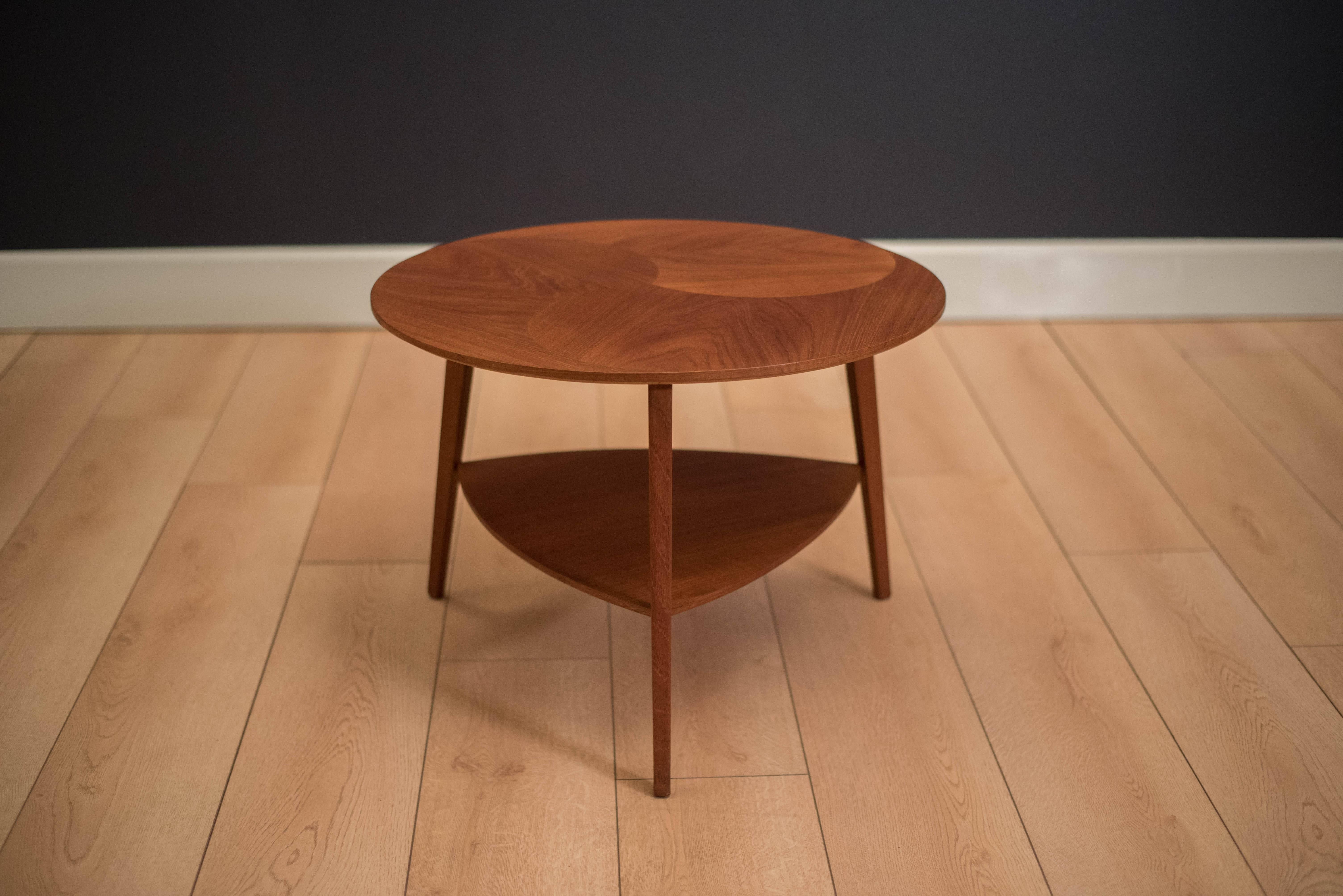 Mid-Century Modern round teak side table manufactured by Mobelintarsia, Denmark. This two-tier piece features a unique round top with a lower triangular shelf.