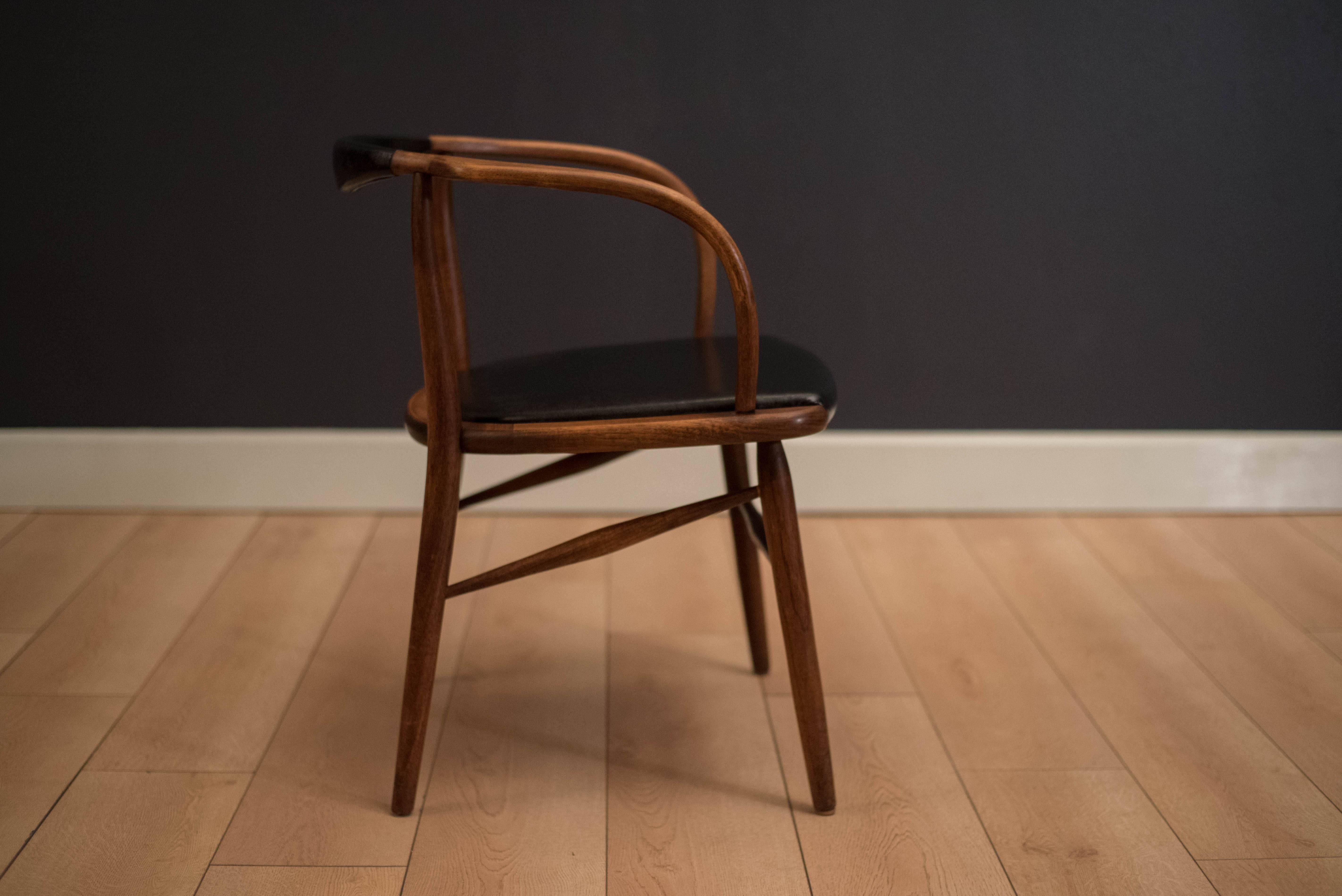 Mid-Century single armchair in walnut, circa 1950s. This piece features unique curved walnut arms and original black Naugahyde upholstery.
