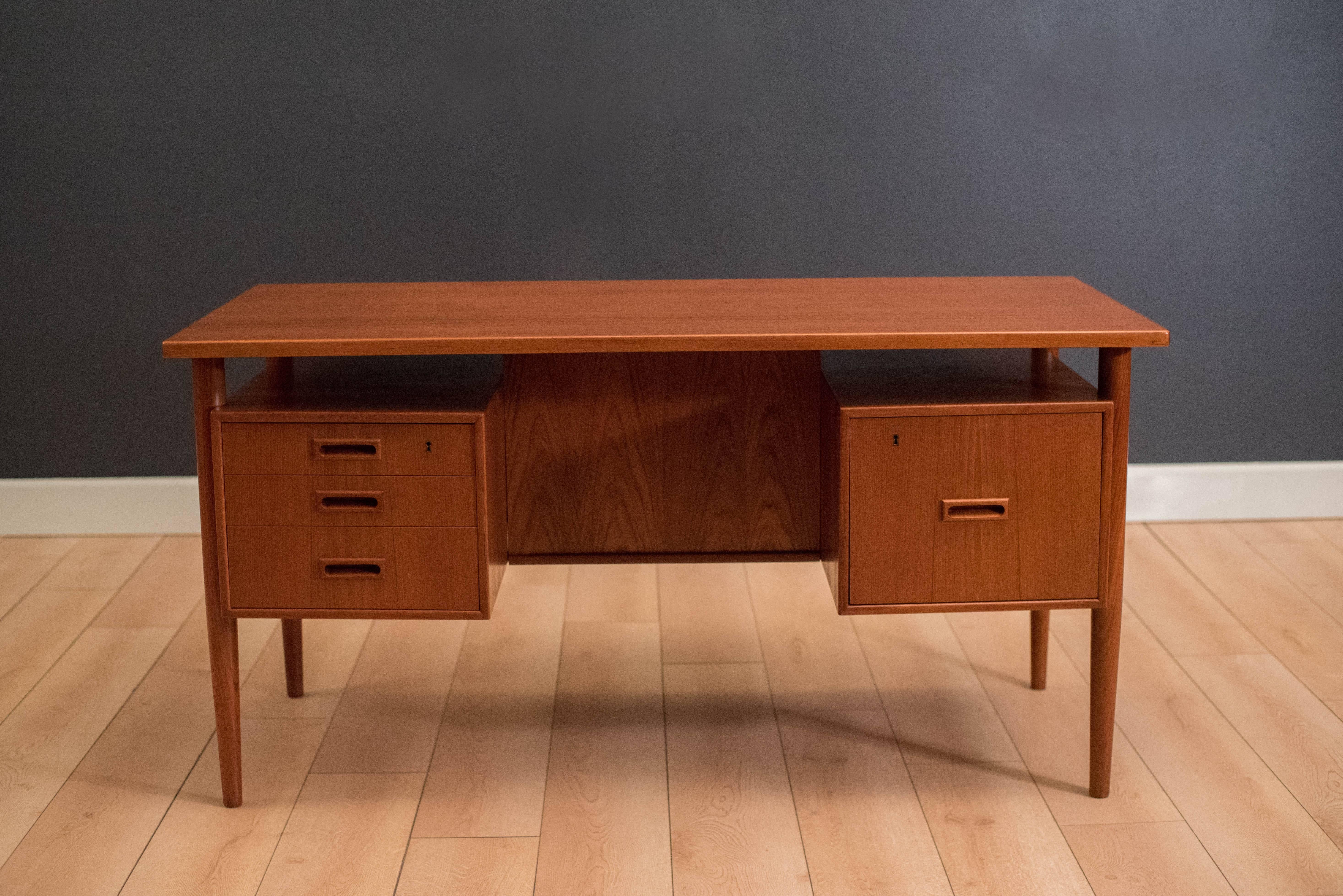 Mid-Century Modern desk in teak, circa 1960s. This piece features a floating desk top with external legs. Includes three small dovetailed drawers and one filing cabinet. Finished on the back with an open bookshelf which allows the desk to be