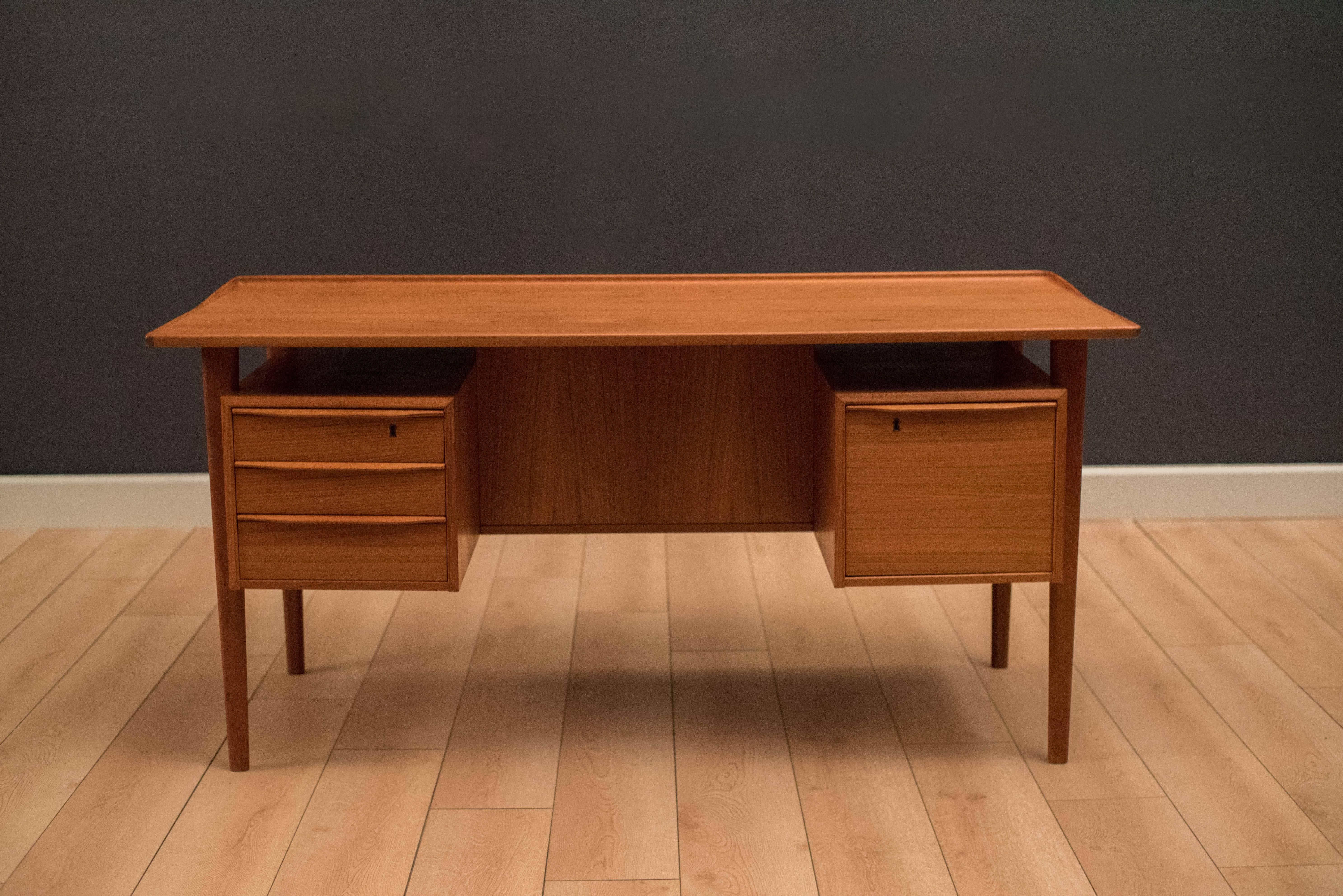 Danish executive desk designed by Peter Lovig Nielsen for Dansk in teak. Features sculpted teak drawer handles and a raised edge top. This piece includes three dovetailed drawers and a file drawer. The back is finished with a bookshelf and can be