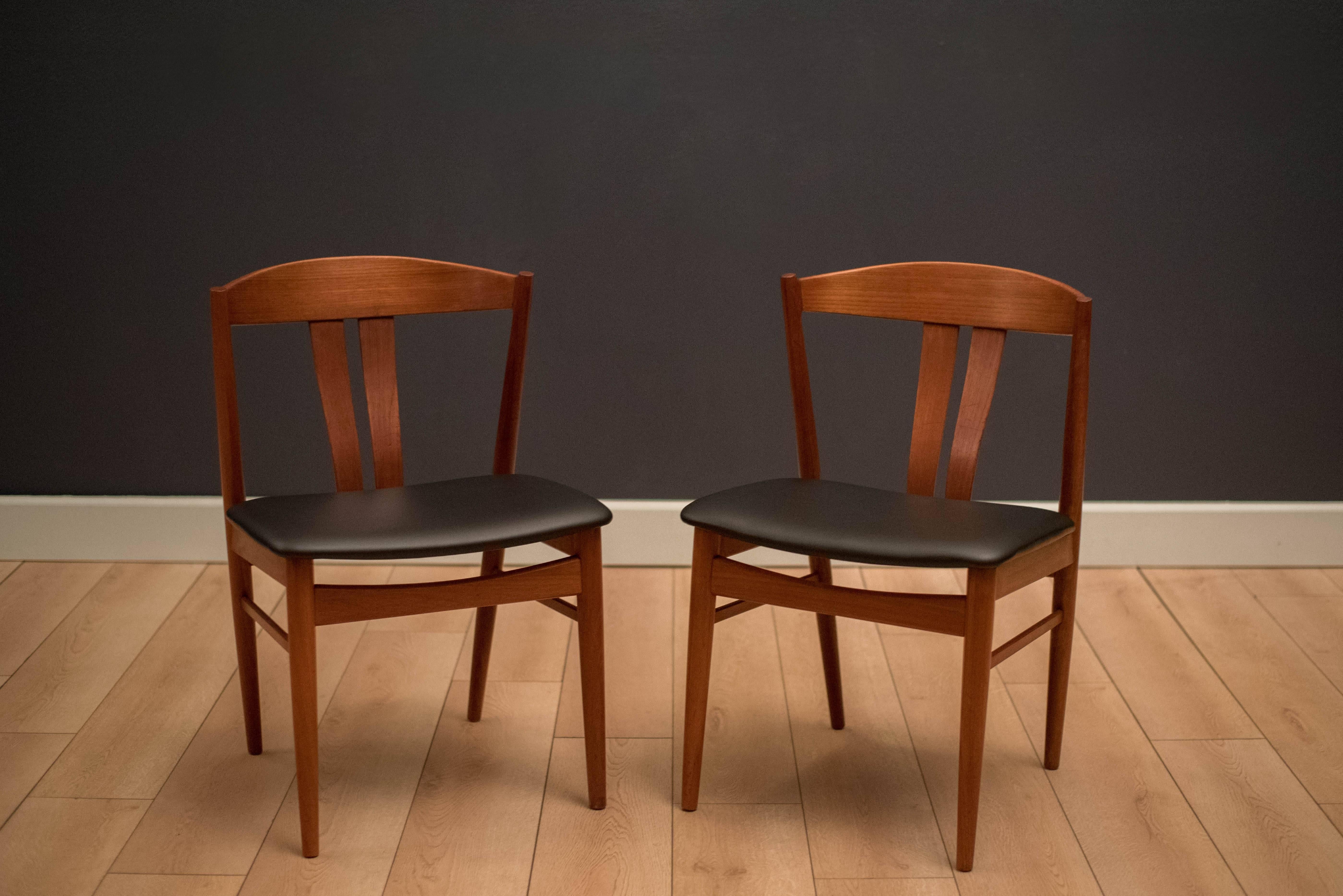 Mid-Century Modern pair of dining chairs by Vejle Stole og Mobelfabrik, Denmark. This set has newly reupholstered seats in black vinyl. Features a sculpted solid teak frame and curved backrest.