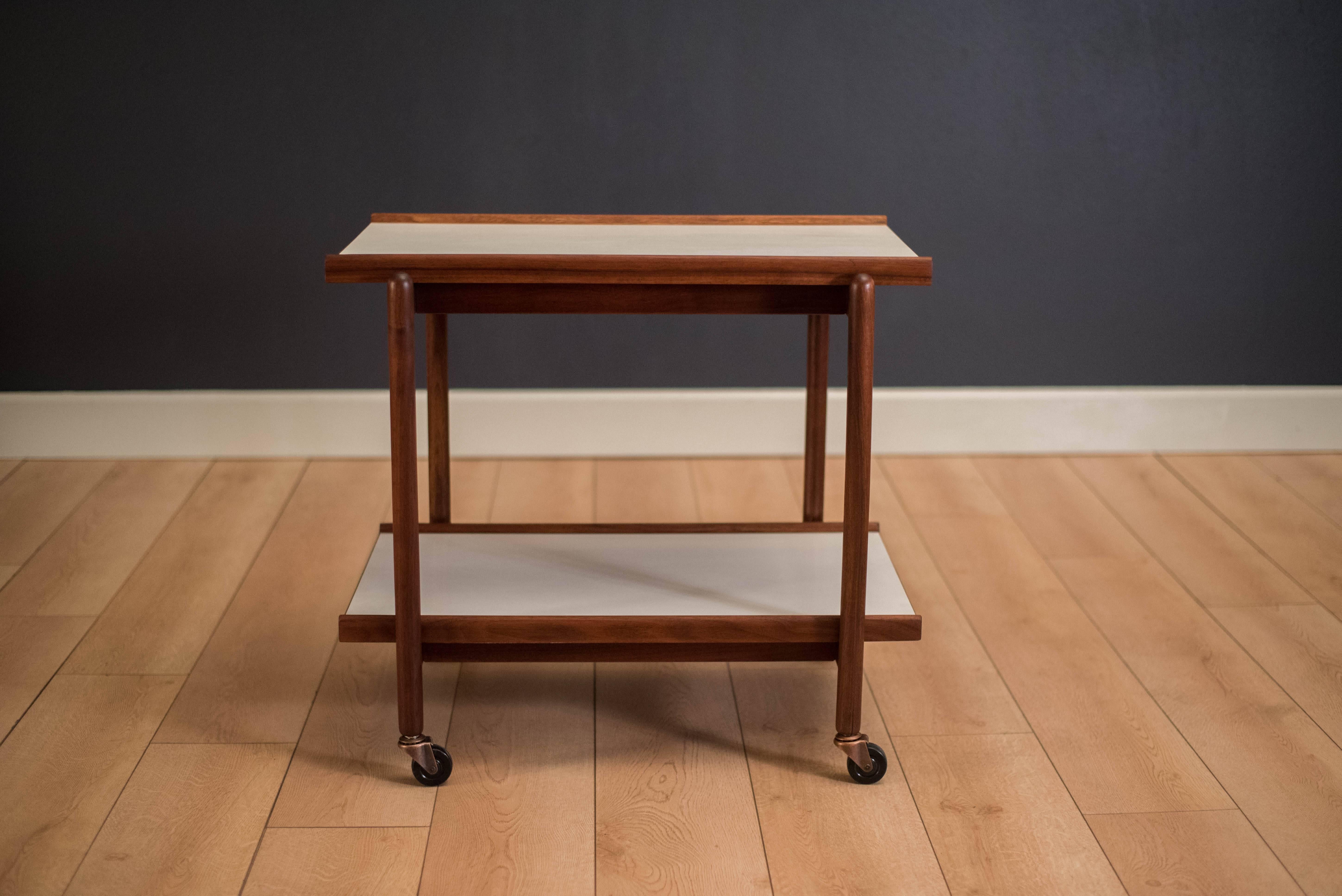 Vintage two-tier rolling bar cart in walnut, circa 1960s. This serving cart includes a raised edge design with white laminate trays for easy maintenance. Bottom tray is removable.