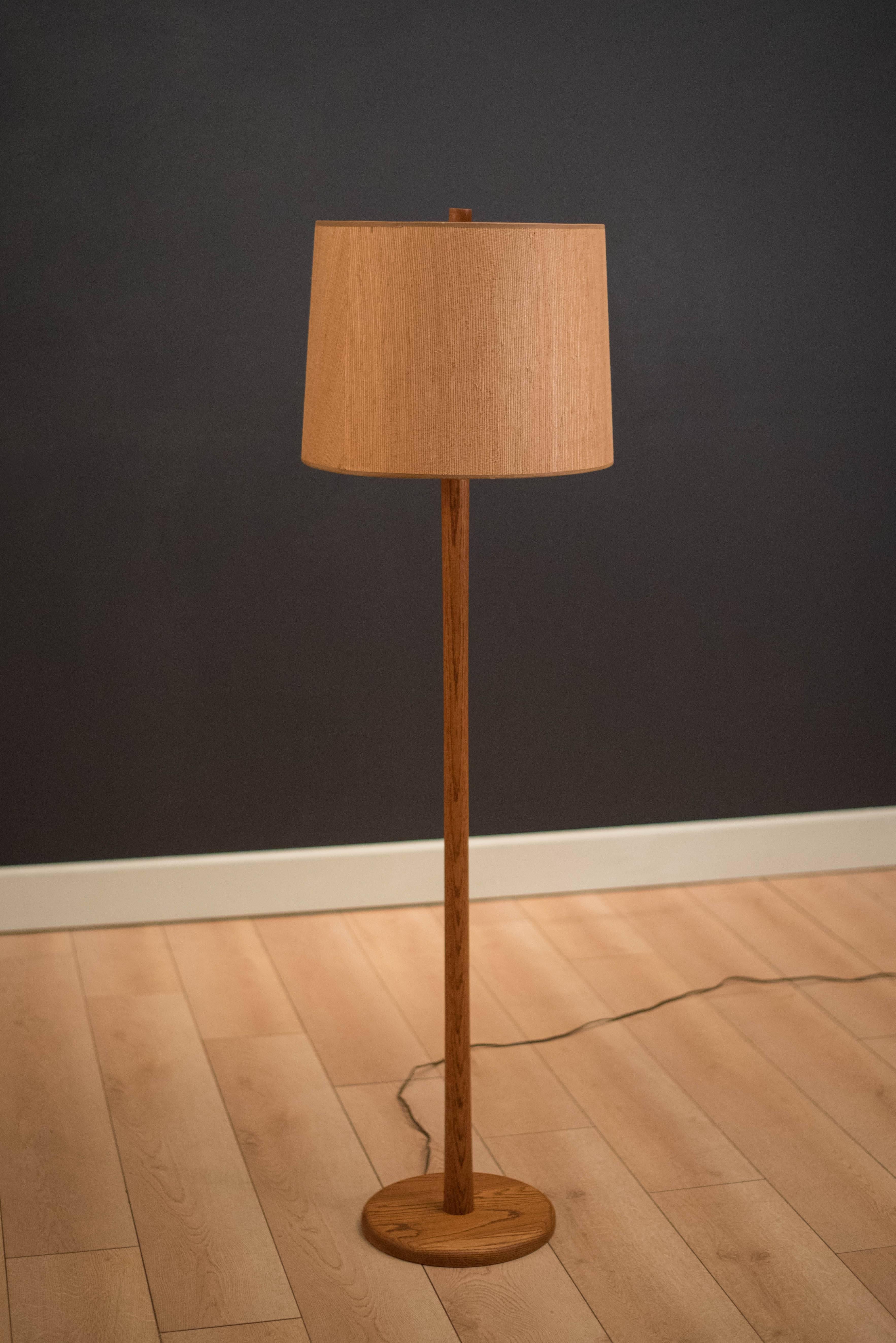 Mid century modern floor lamp in oak designed by Jane and Gordon Martz for Marshall Studios. Features a three-way switch and includes grasscloth drum shade and signature wood finial.