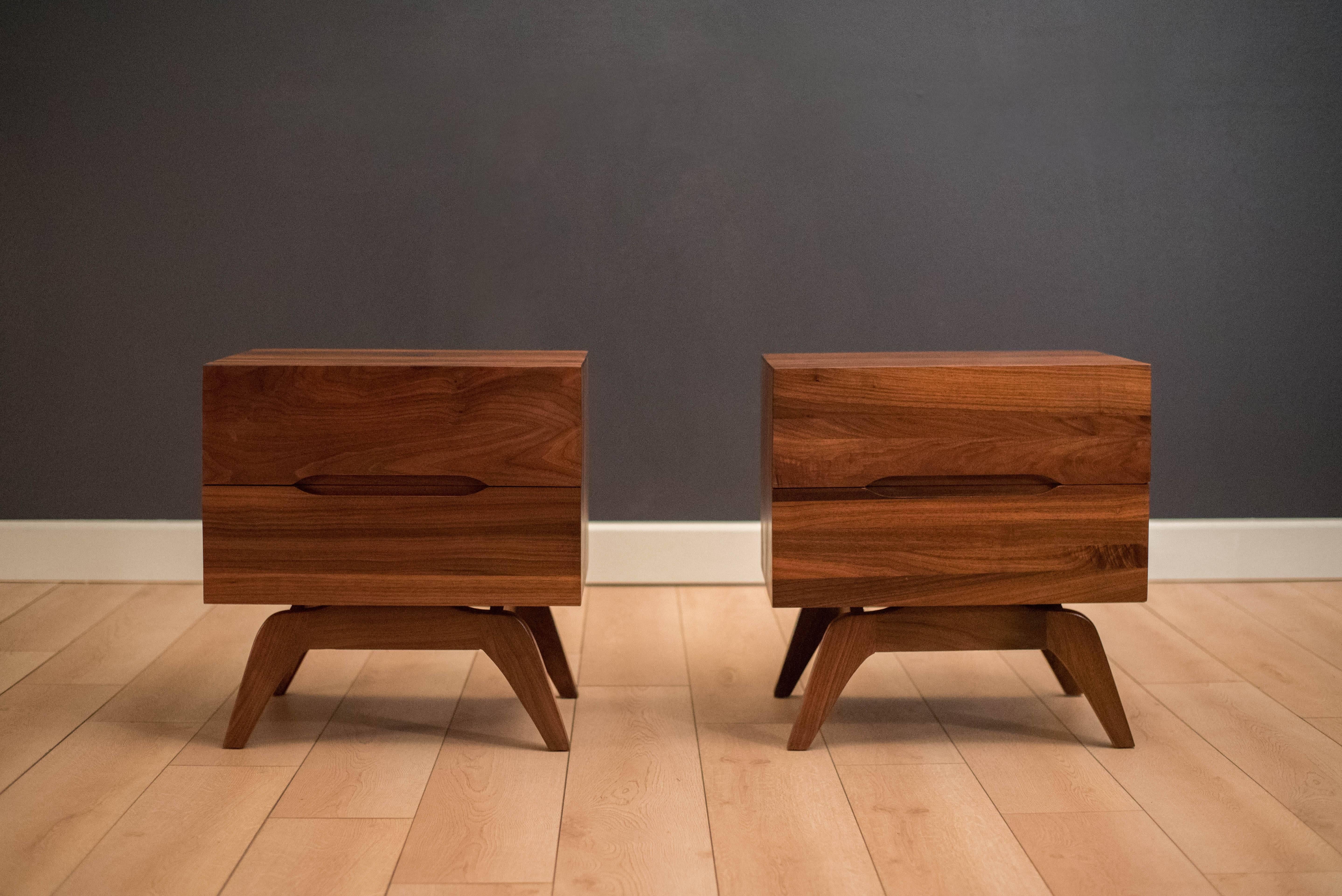 Vintage matching pair of nightstands in solid planked walnut, circa 1960s. This set features a unique sculpted base and includes two storage drawers with inset pulls. Price is for the set.