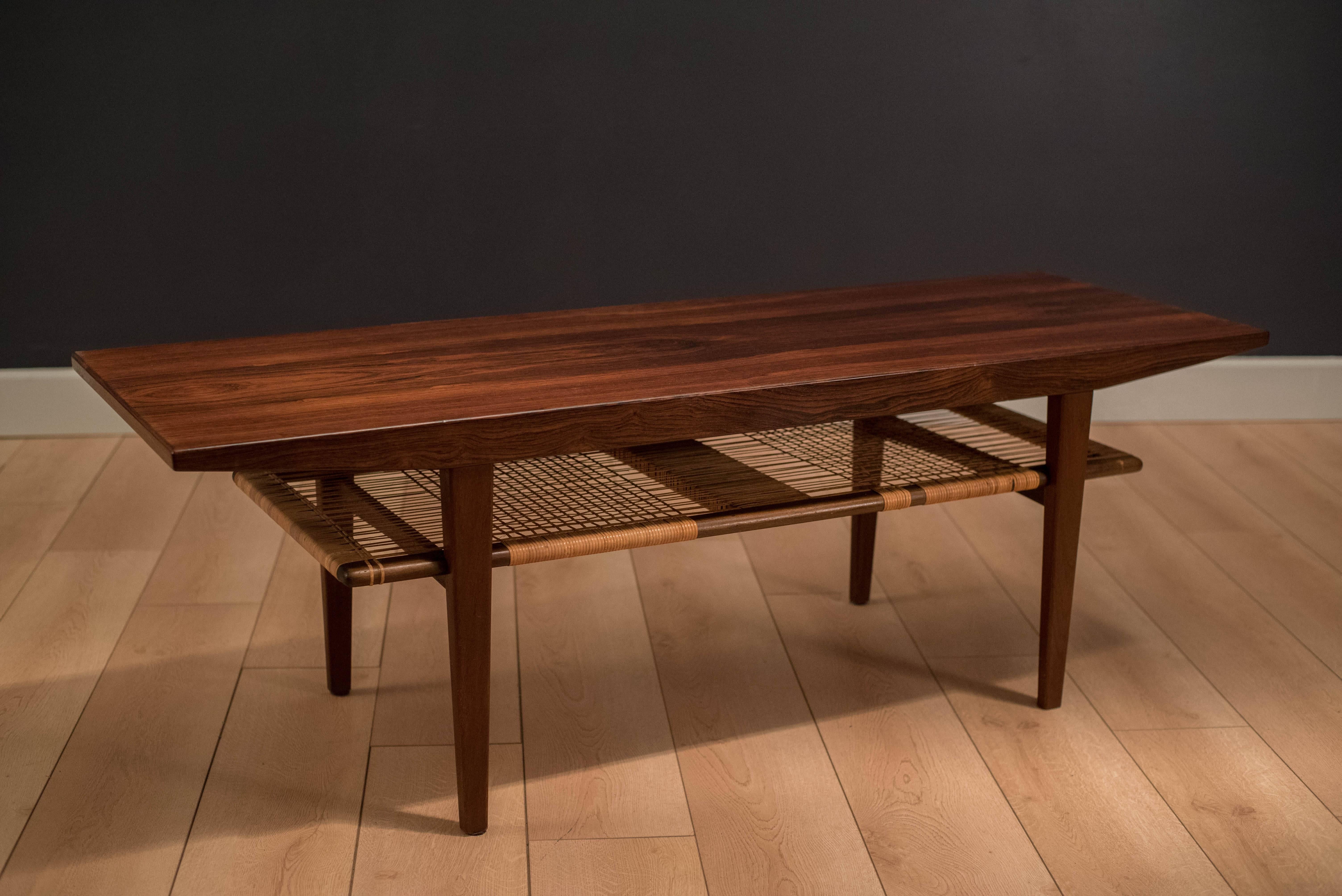 Vintage Danish Two-Tier Coffee Table in rosewood. This piece features a lower tier magazine rack. Caning is intact. 