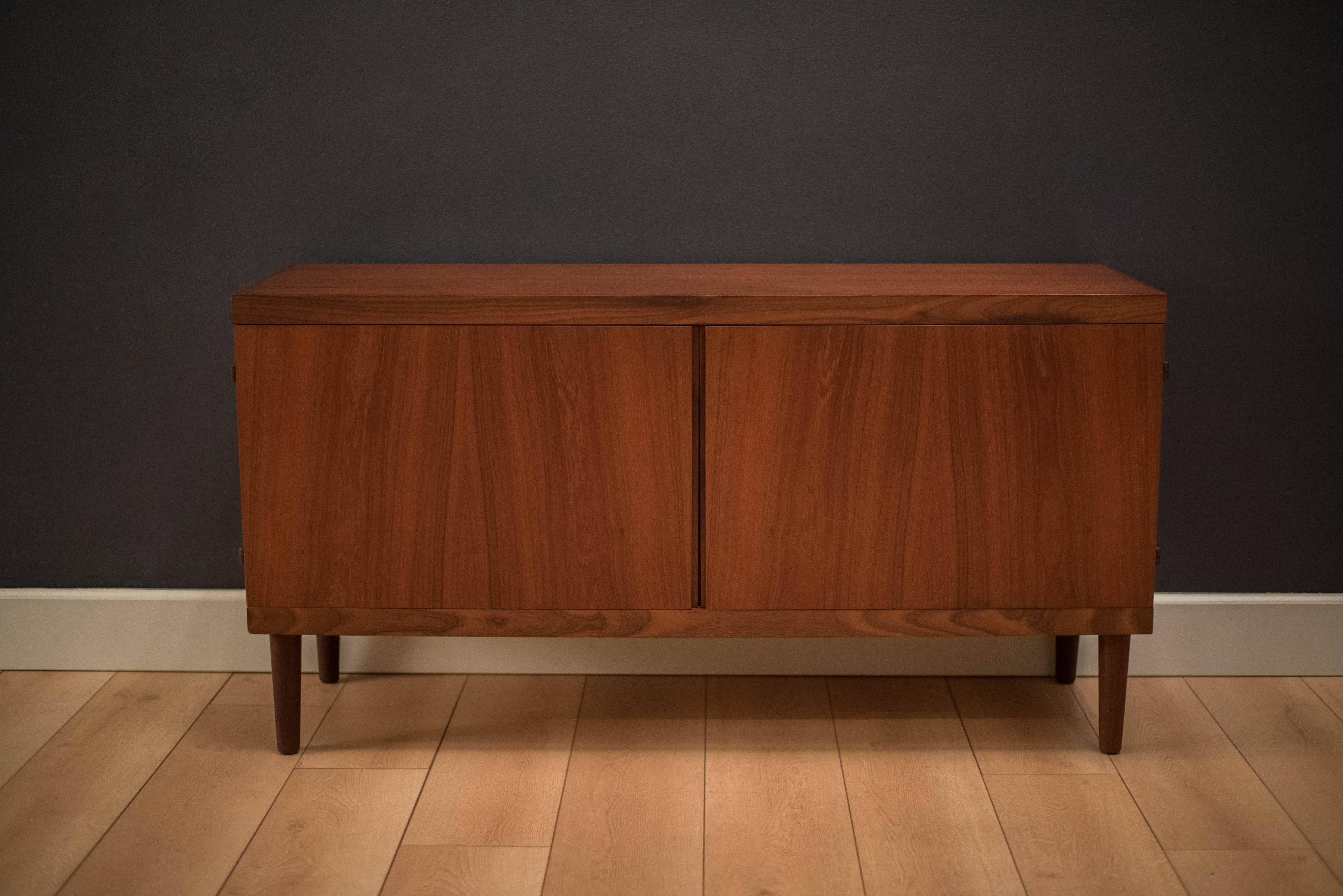 Mid-Century Danish teak credenza by Hans Olsen. This beautifully crafted piece displays opposing teak veneers and brass hardware. Doors swing open to reveal adjustable shelving. Functions as an entertainment console or buffet.

 