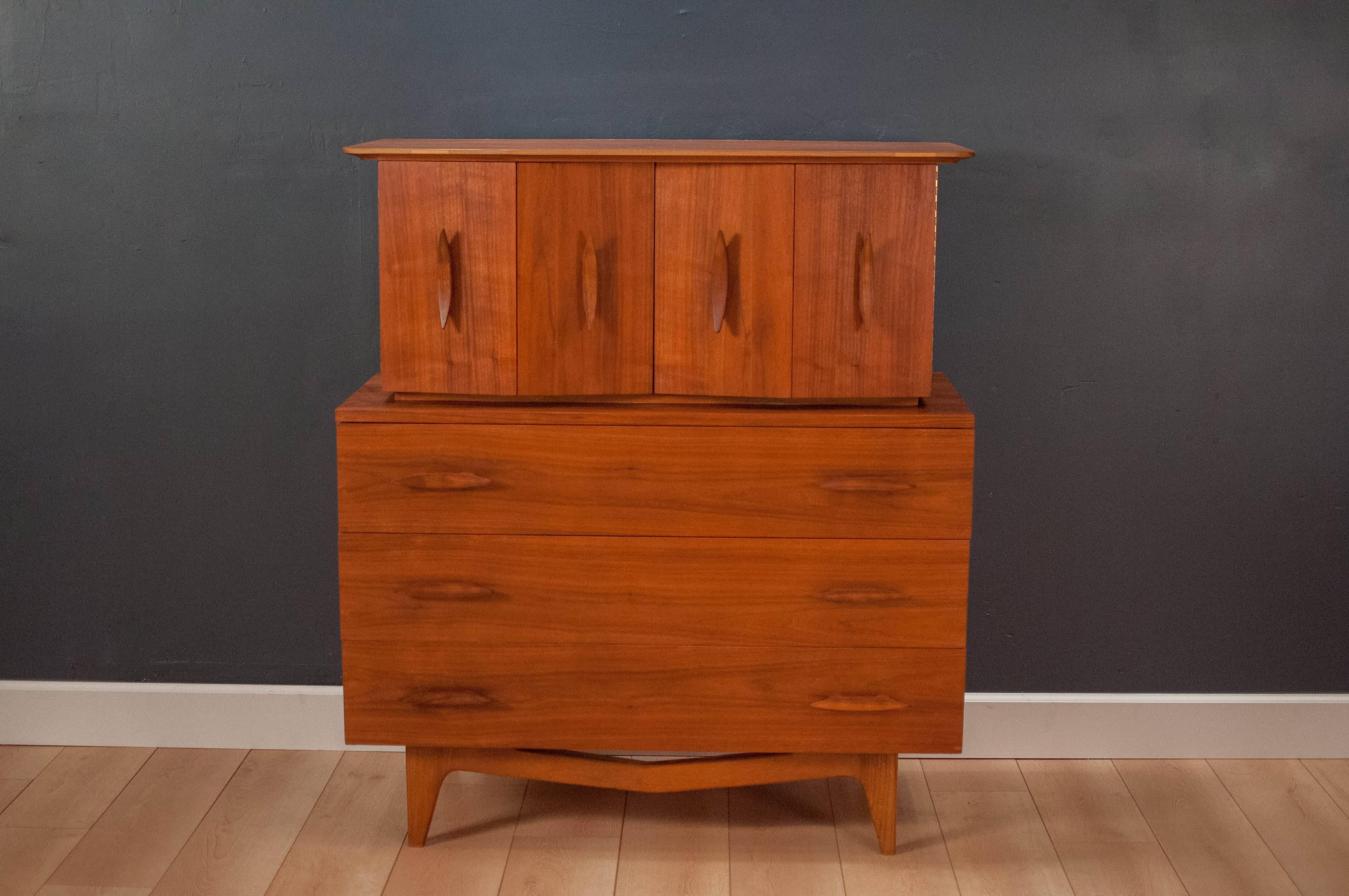 Mid-Century Tall Dresser in walnut c. 1950's. This unique piece features sculpted solid wood handles and atomic style legs. Equipped with seven deep storage drawers. 

