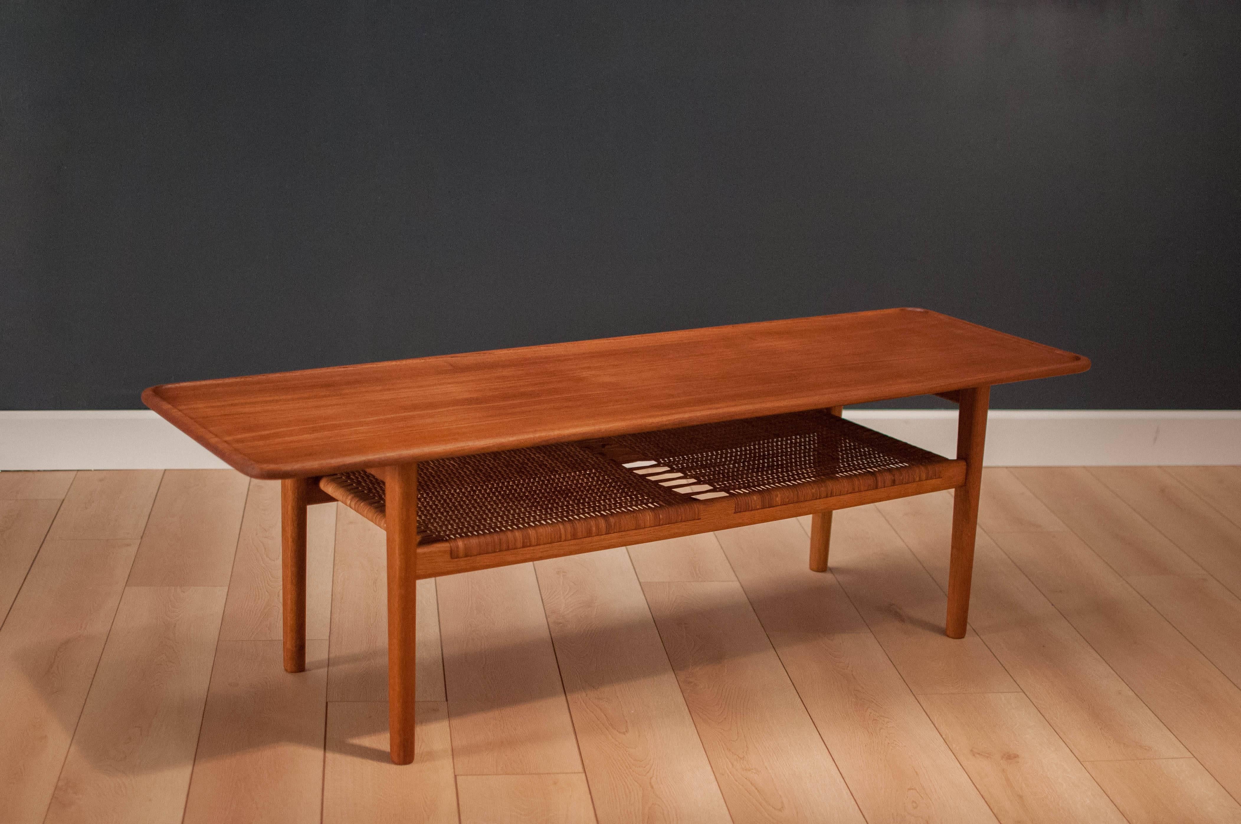 Danish teak coffee table by Hans J. Wegner for Andreas Tuck. This piece displays a gorgeous sculpted solid teak top and oak base. Features lower tier magazine rack for extra storage and caning is intact. 

   