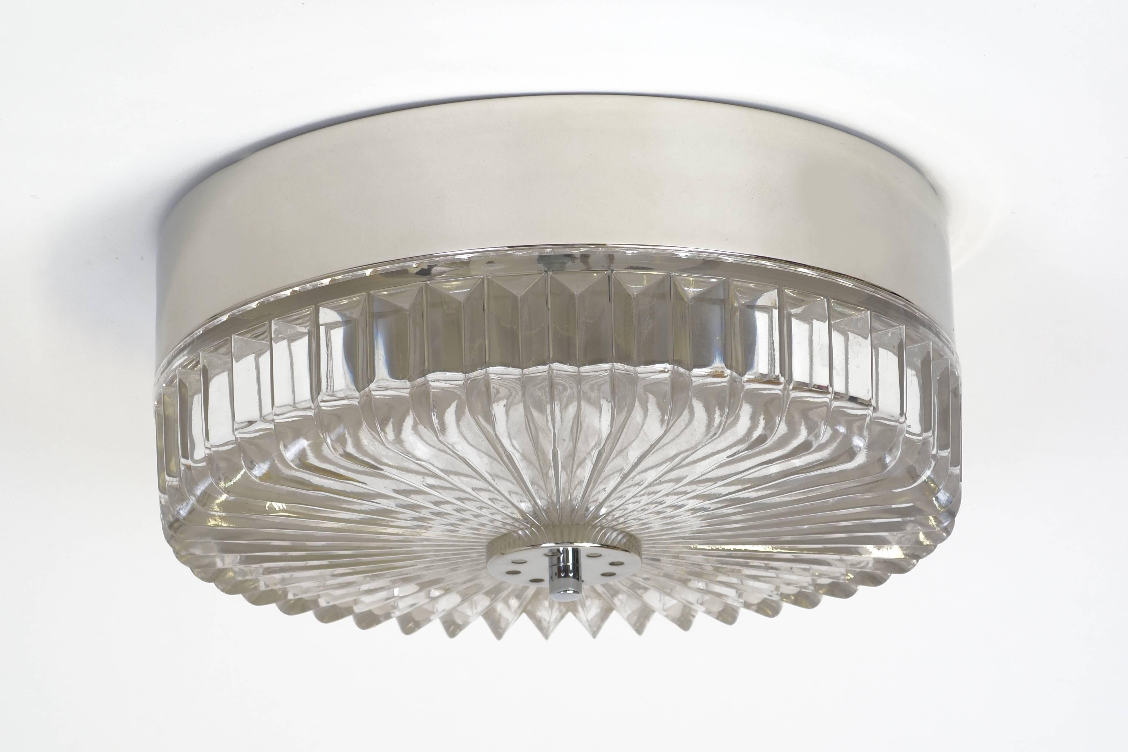 Preciously appearing ceiling lamp in the shape of a turbine wheel. The metal sheath is of nickel plated aluminium and has three bulbs within. The fluted glass disc is made of one single piece, fixed with a non-visible screw nut in the middle. Very