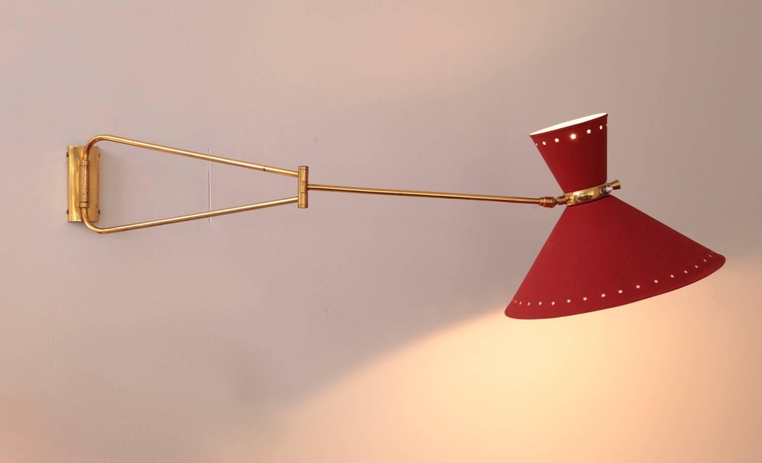 Fully original arm wall light by Rene Mathieu for Lunel, double cone lamp shade in original red lacquer with two-light source and individual on/off switches at the center of the shades, brass accent to the arm and star perforation to the shades,