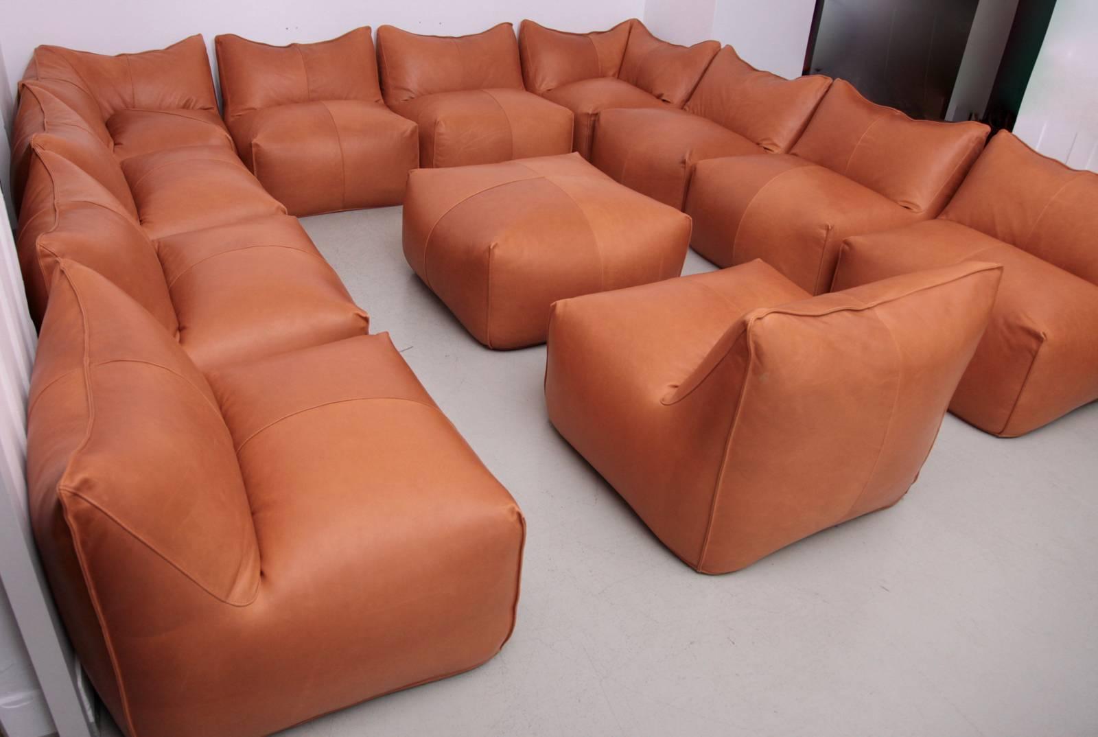 New upholstered set with two corner pieces, nine side and one ottoman pouf. The set is upholstered in a high quality aniline tan leather. We had to replace some of the bottom fabrics due to condition. It is also possible to connect the pcs with each